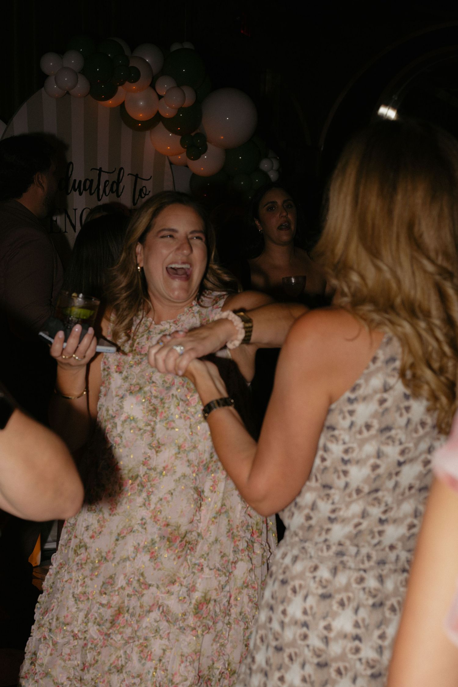 Women laughing and dancing joyfully at a wedding reception party with balloon decorations in background.