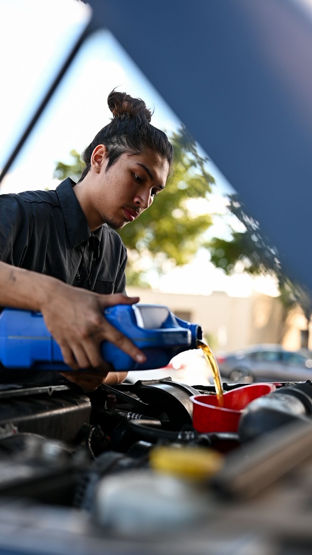 Automotive technician working on engine components in bright daylight.