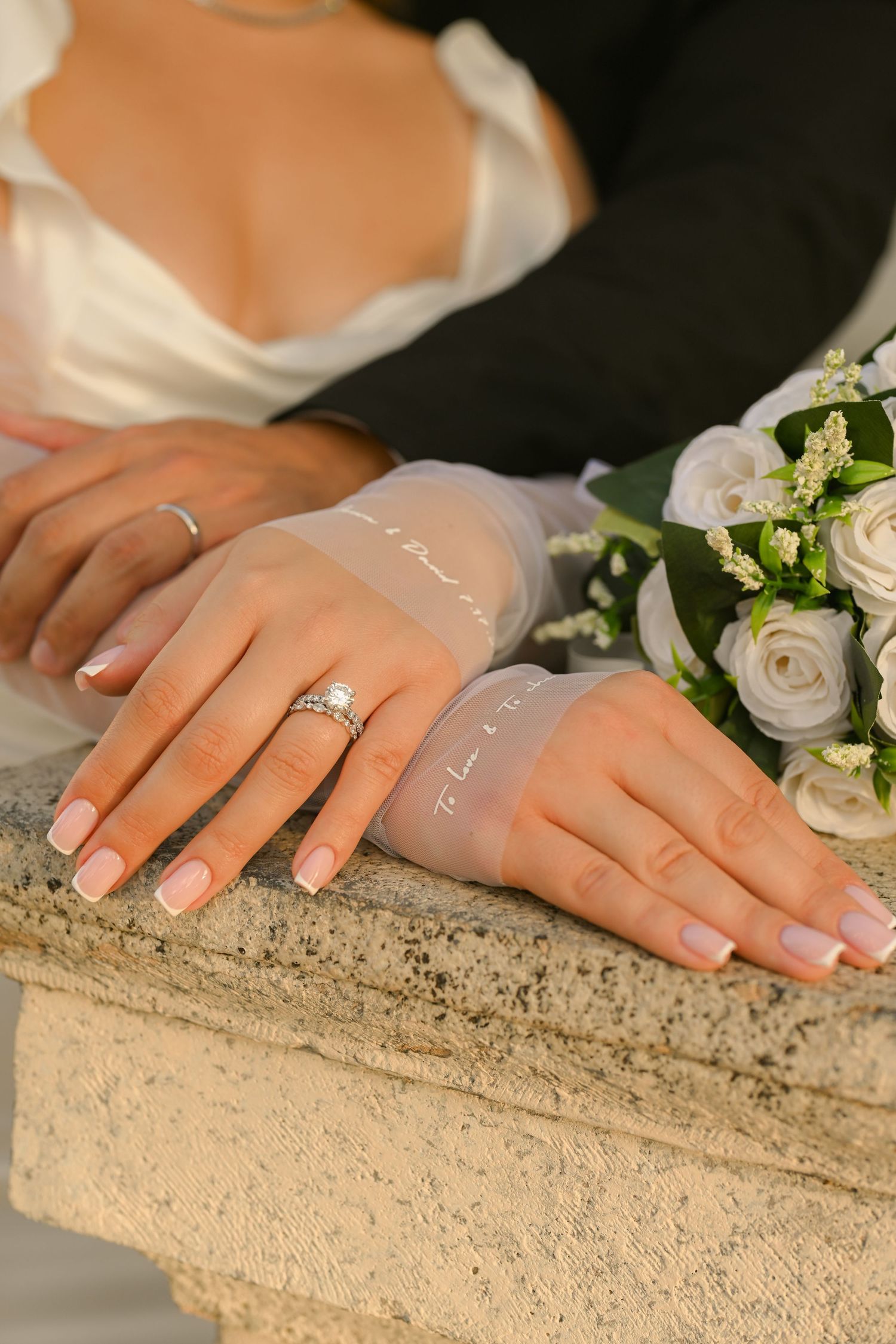 Detail shots of hands wearing wedding rings against white dress fabric.