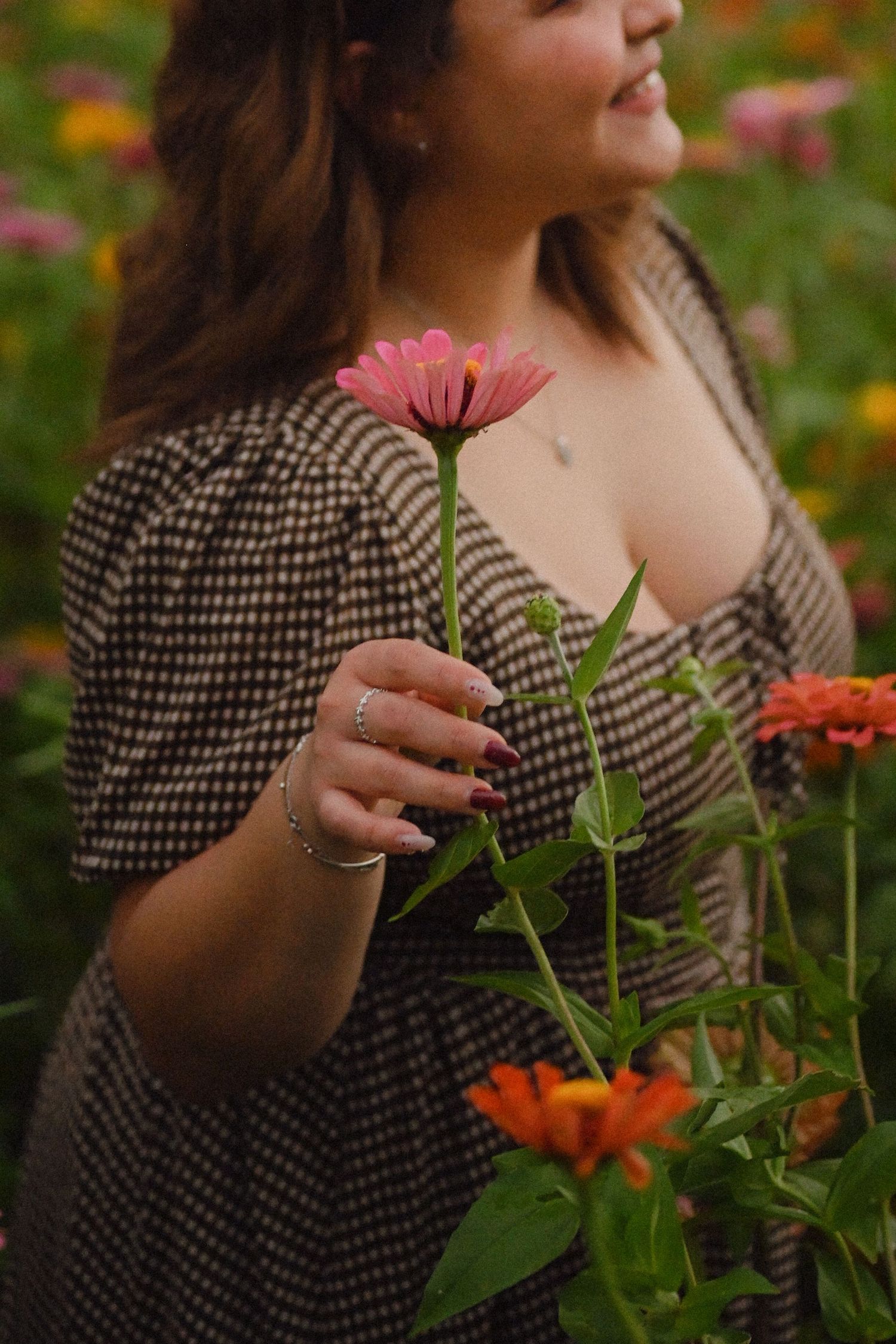 A person in a polka dot dress gently touches pink and orange flowers in a garden setting.