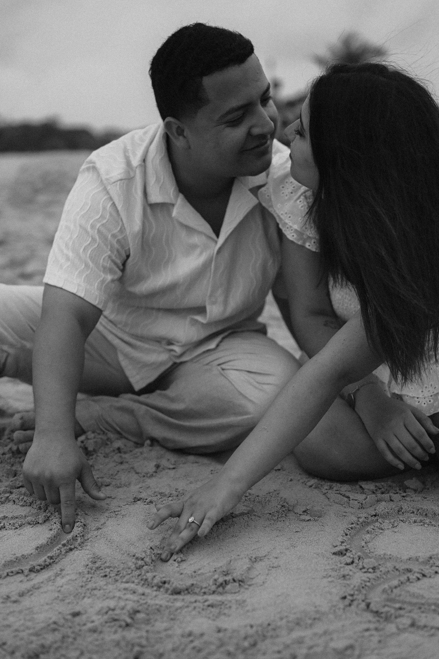 A couple lying in the sand sharing intimate moments in black and white photography.