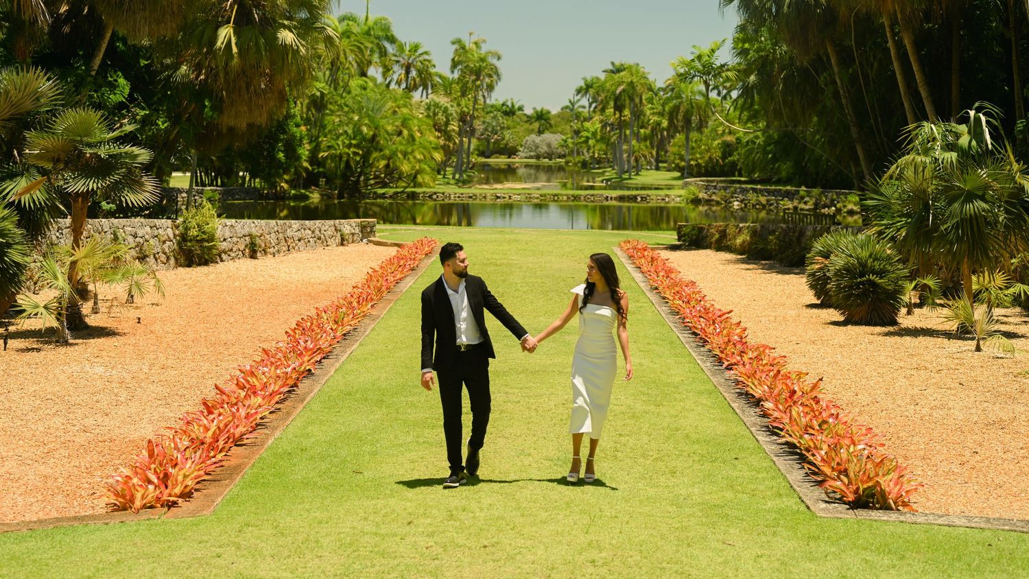 A scenic garden pathway lined with coral flowers and palm trees stretches into the distance.