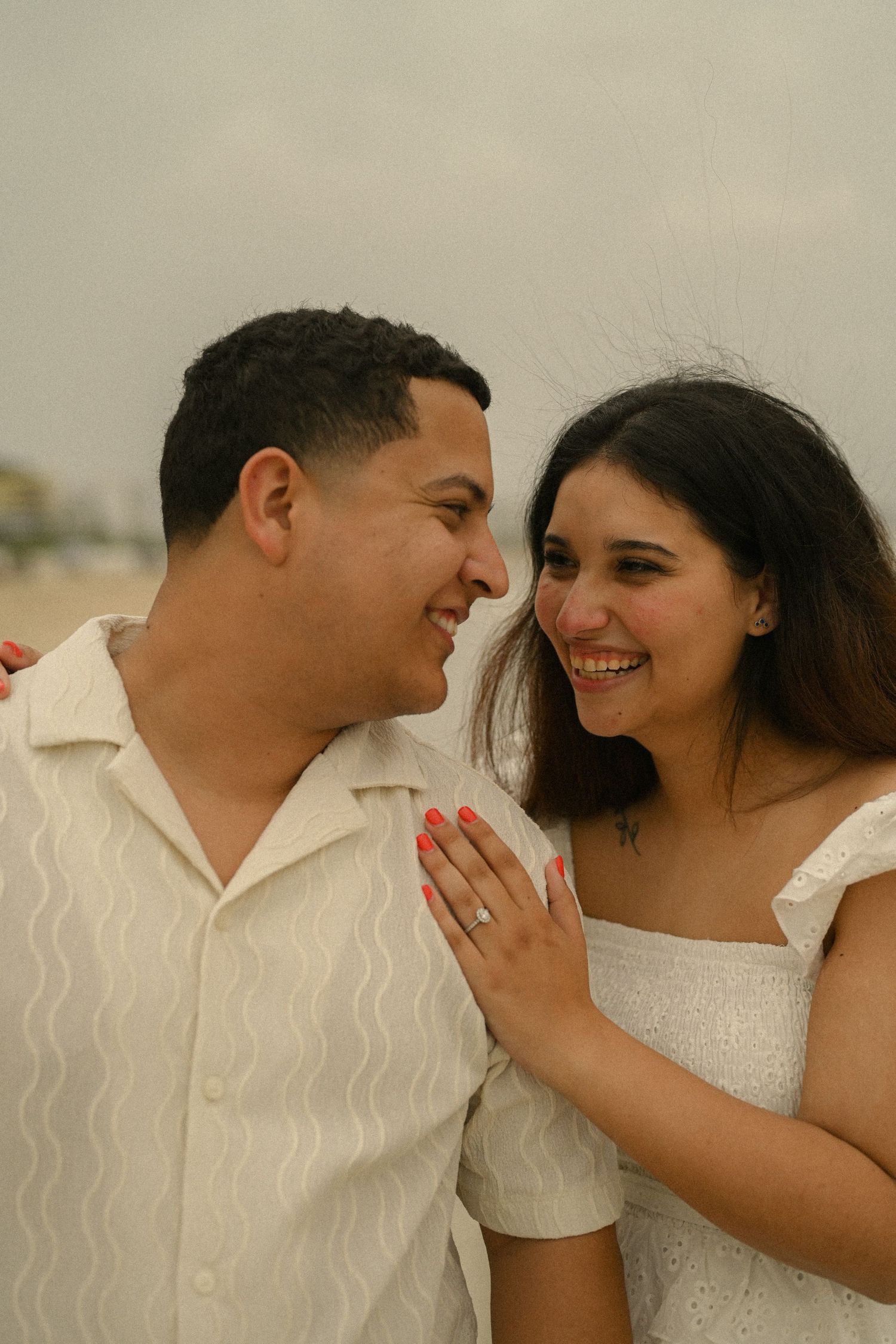 A romantic couple in white outfits sharing intimate moments and laughter at the beach.