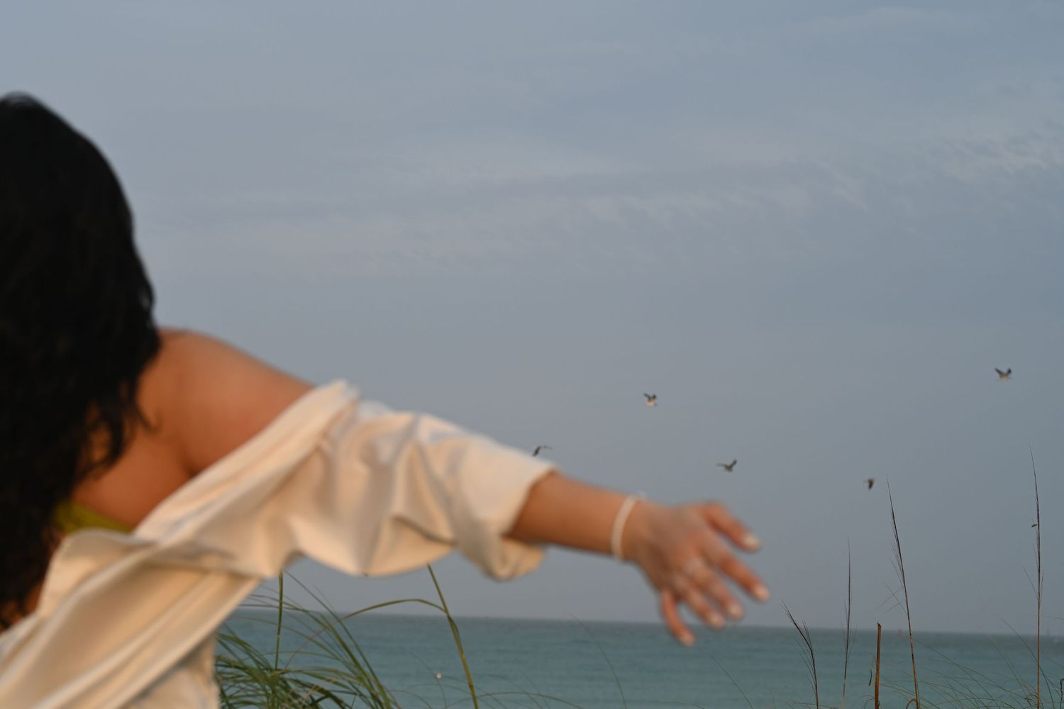 Person in white clothing stretches arms by the ocean.