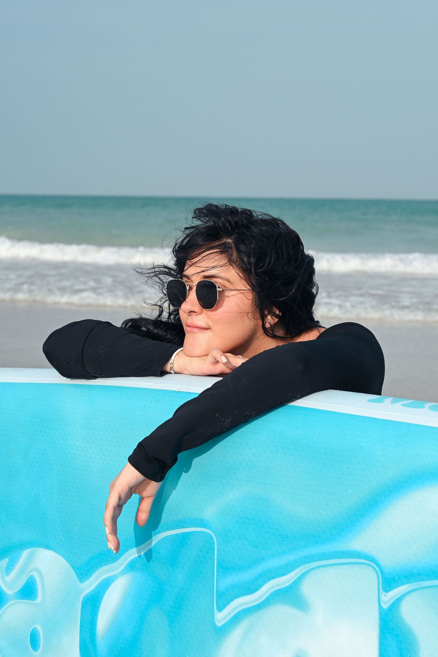 Person in black resting on bright blue surfboard at the beach.