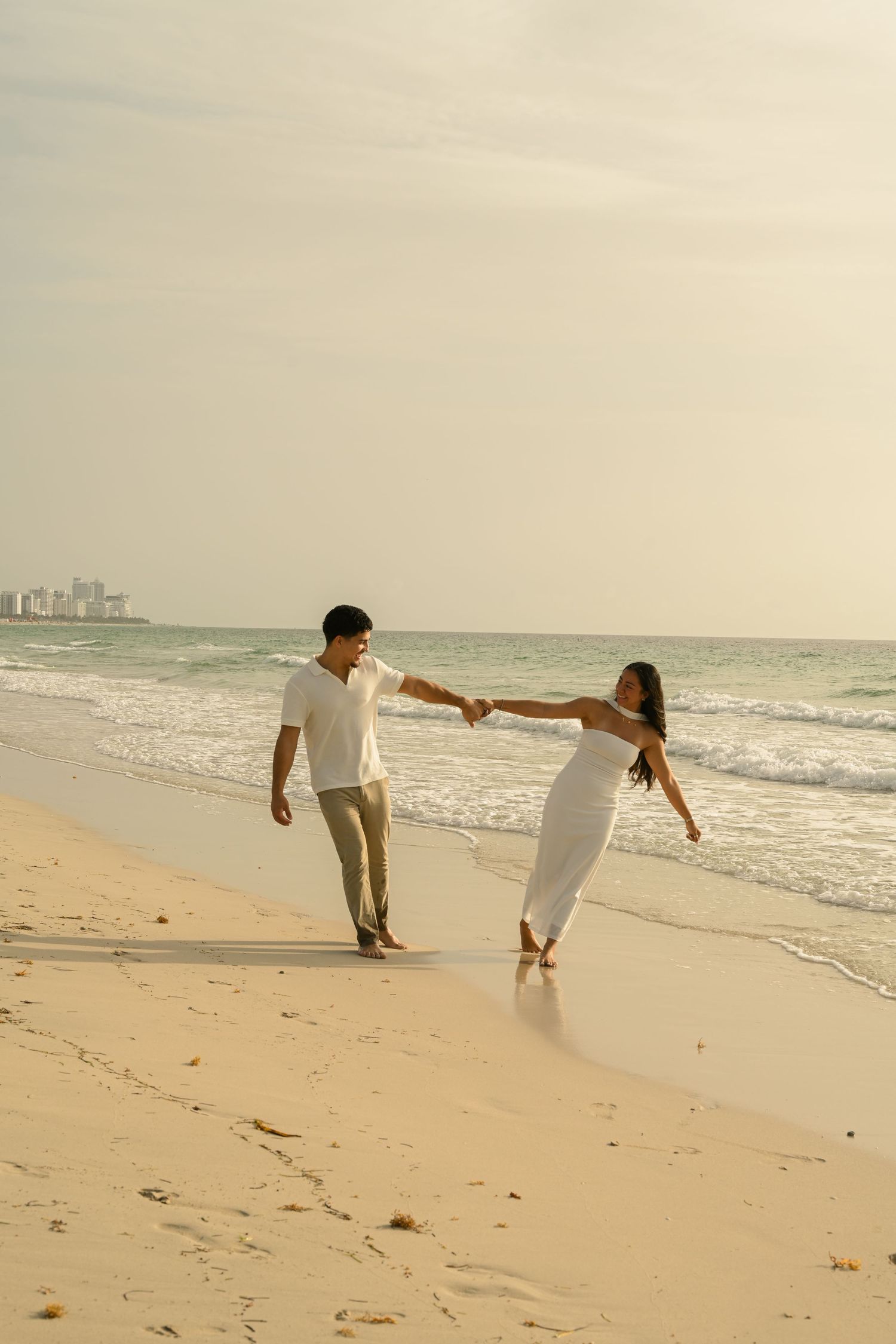 Two people hold hands and lean away from each other playfully on a beach.