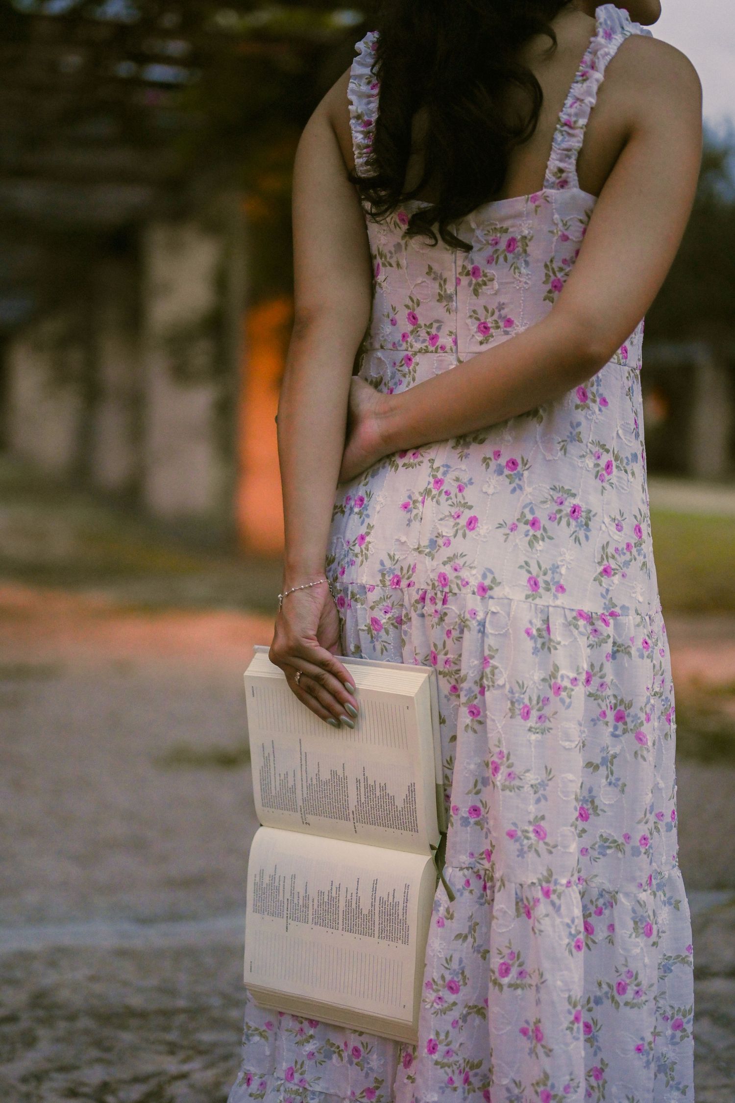 Someone holds a book while wearing a flowing floral dress in an architectural setting.