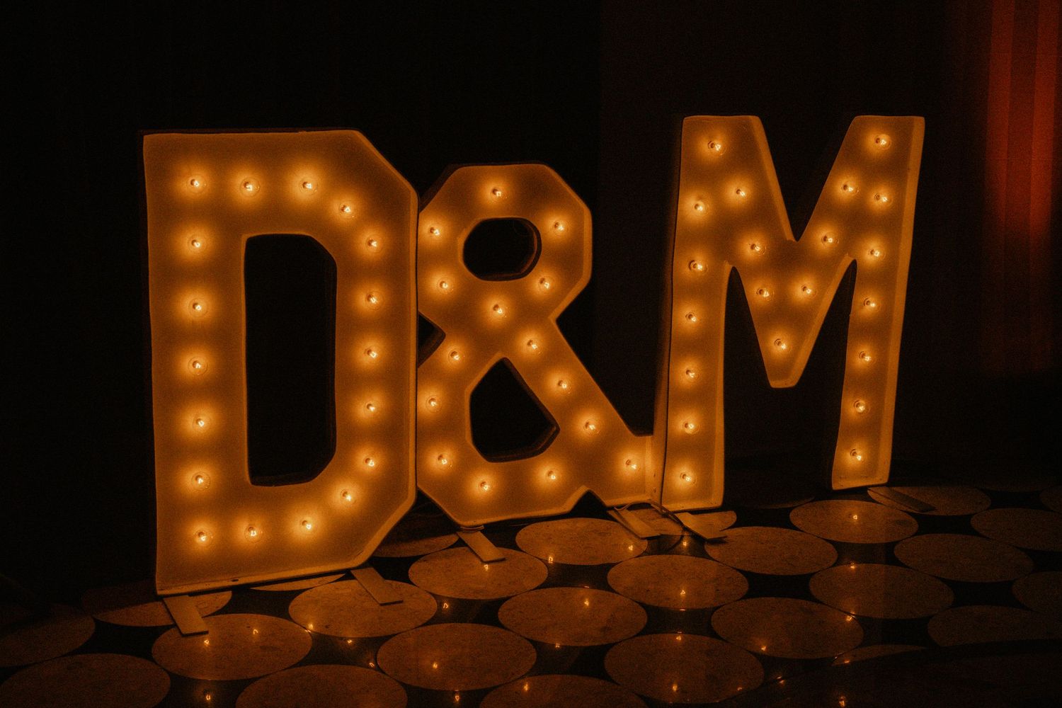 Illuminated marquee letters D&M surrounded by candles at a wedding reception.