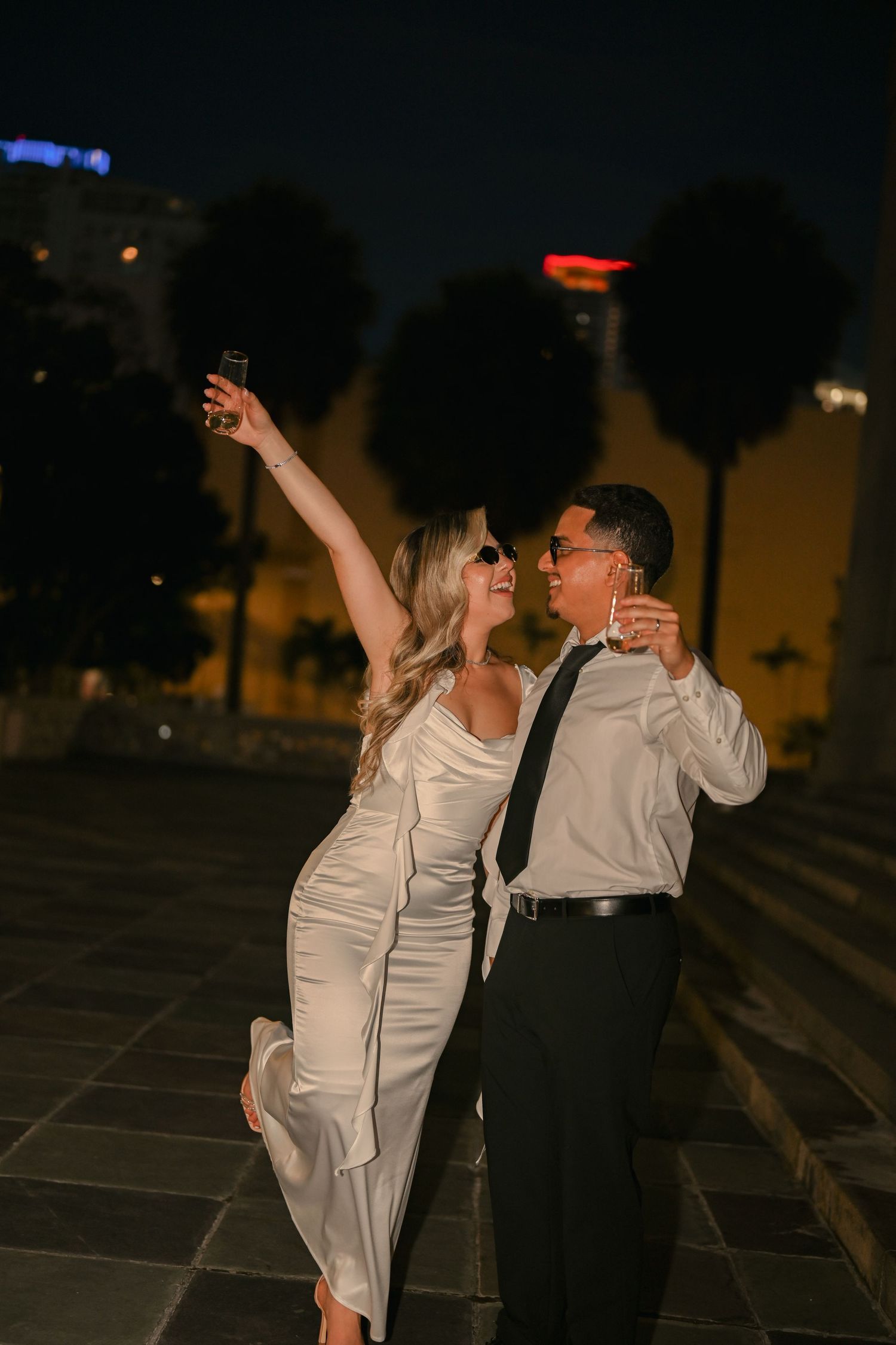Two people dance together outdoors at dusk, one in a white dress and one in dark formal wear.