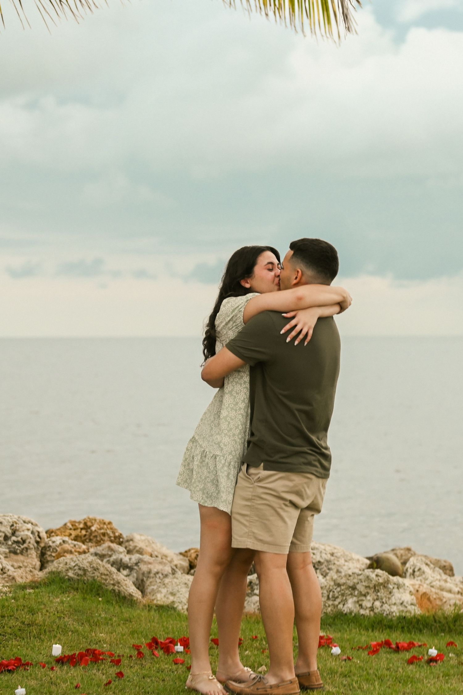 A newly engaged couple embraces on a cliff overlooking the ocean.