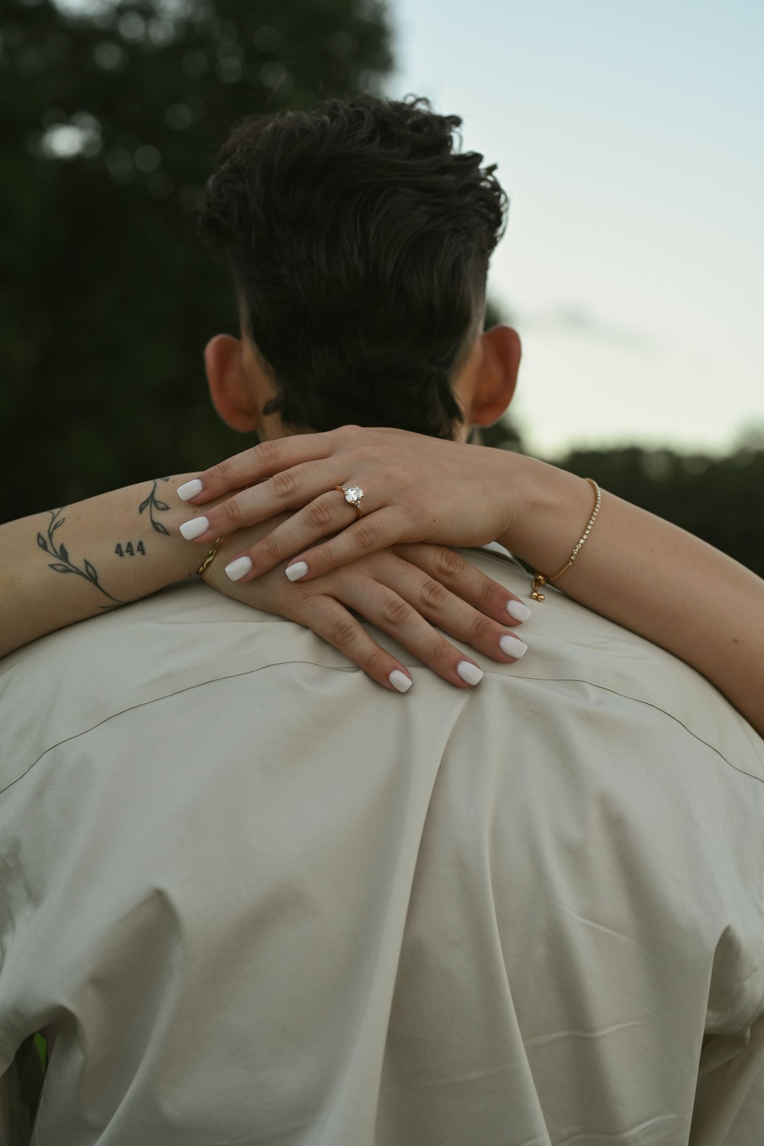 Close-up of hands with tattoos and rings embracing during an intimate outdoor photoshoot.