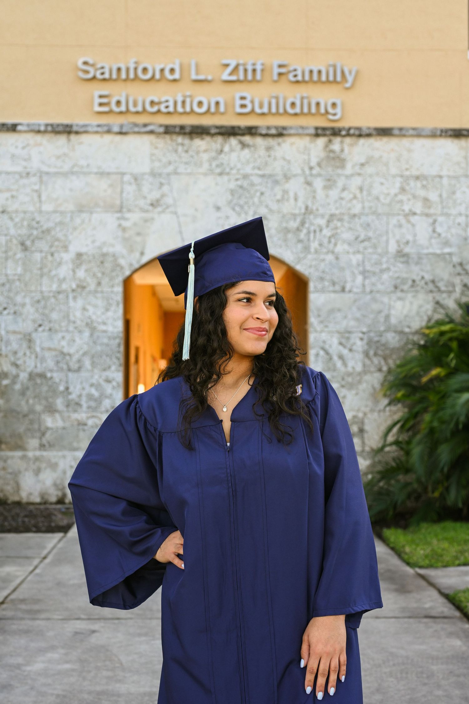 Graduate in navy cap and gown poses in front of Sanford L. Ziff Family Education Building.
