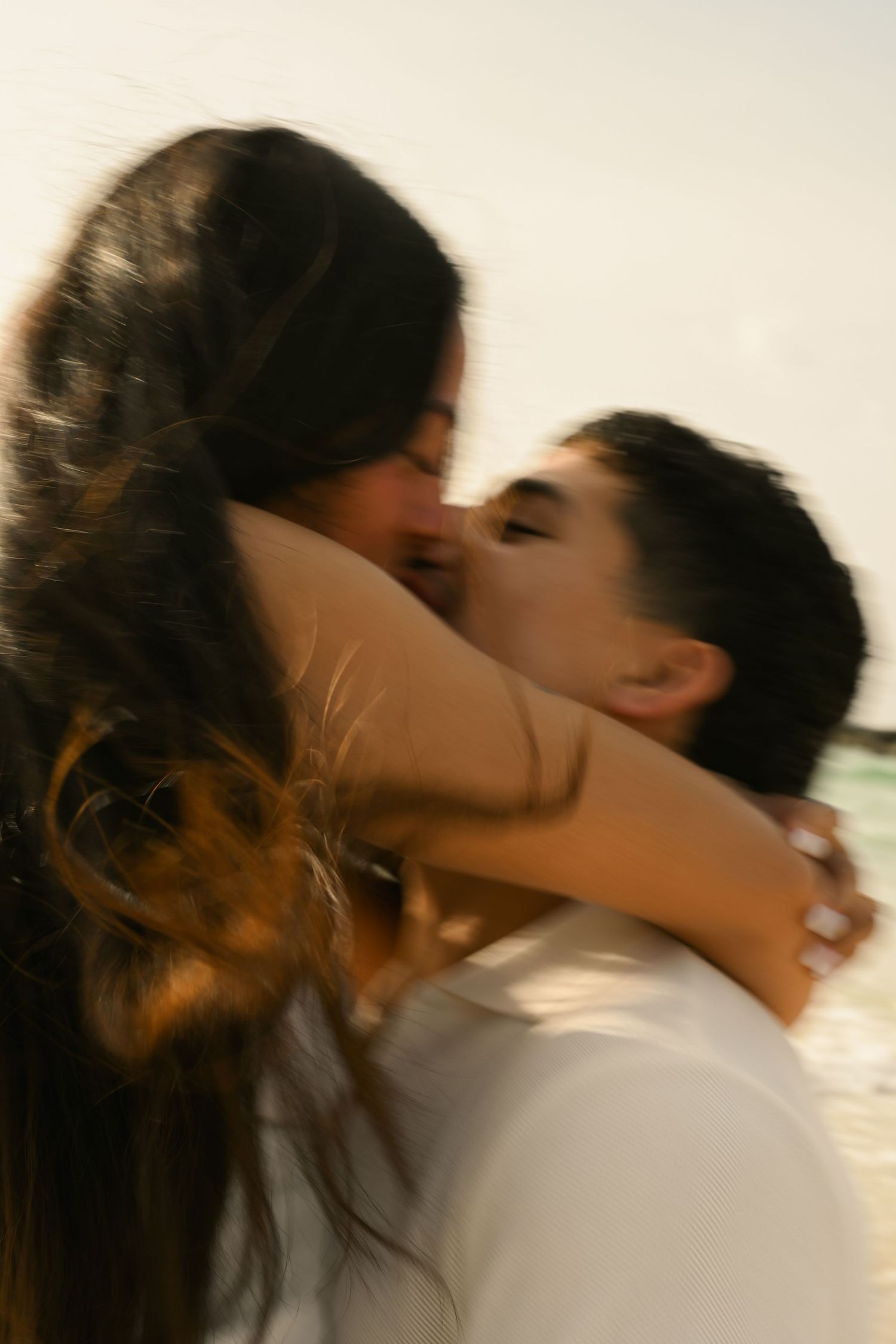 Couple sharing a romantic kiss on the beach, embracing each other tenderly in a blurred motion shot.