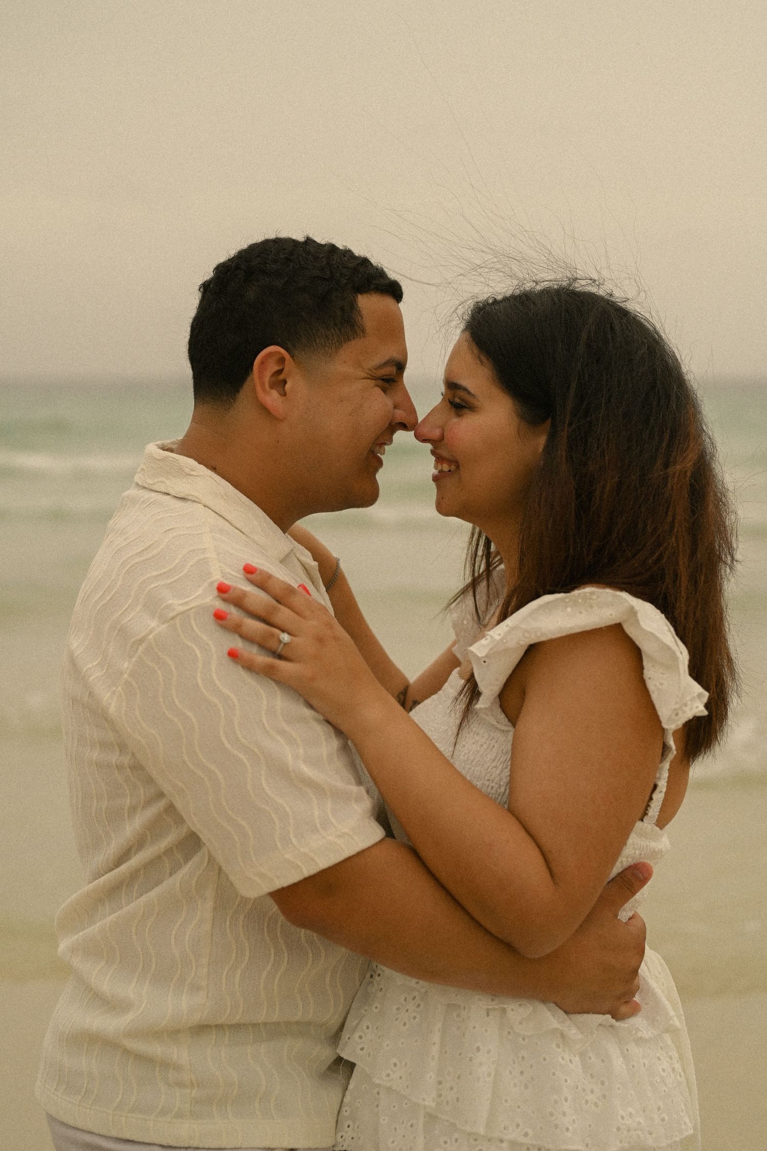 A romantic beach portrait of a couple in white sharing an intimate moment by the ocean.