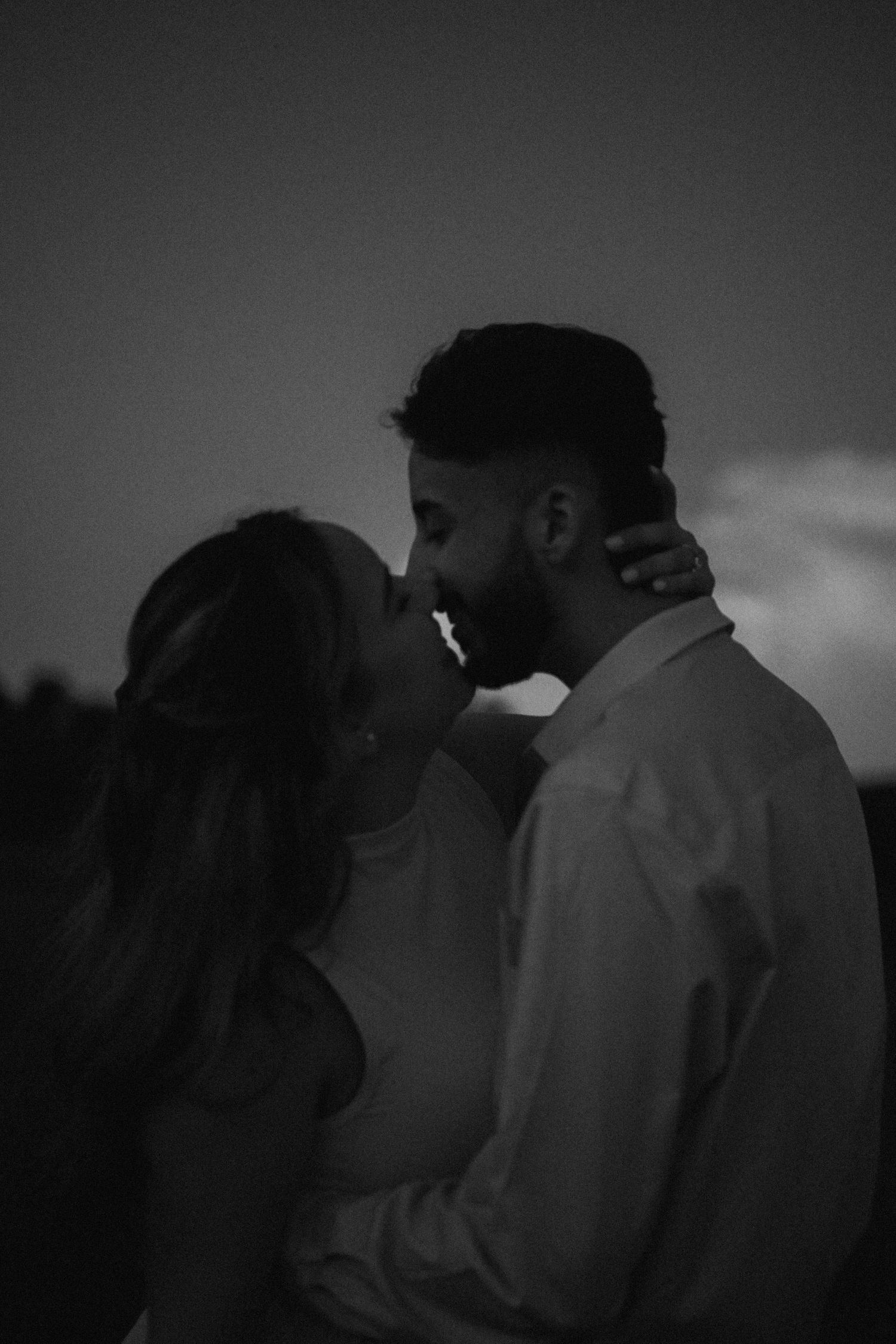 Silhouette of a couple sharing a tender moment against a darkening sky.