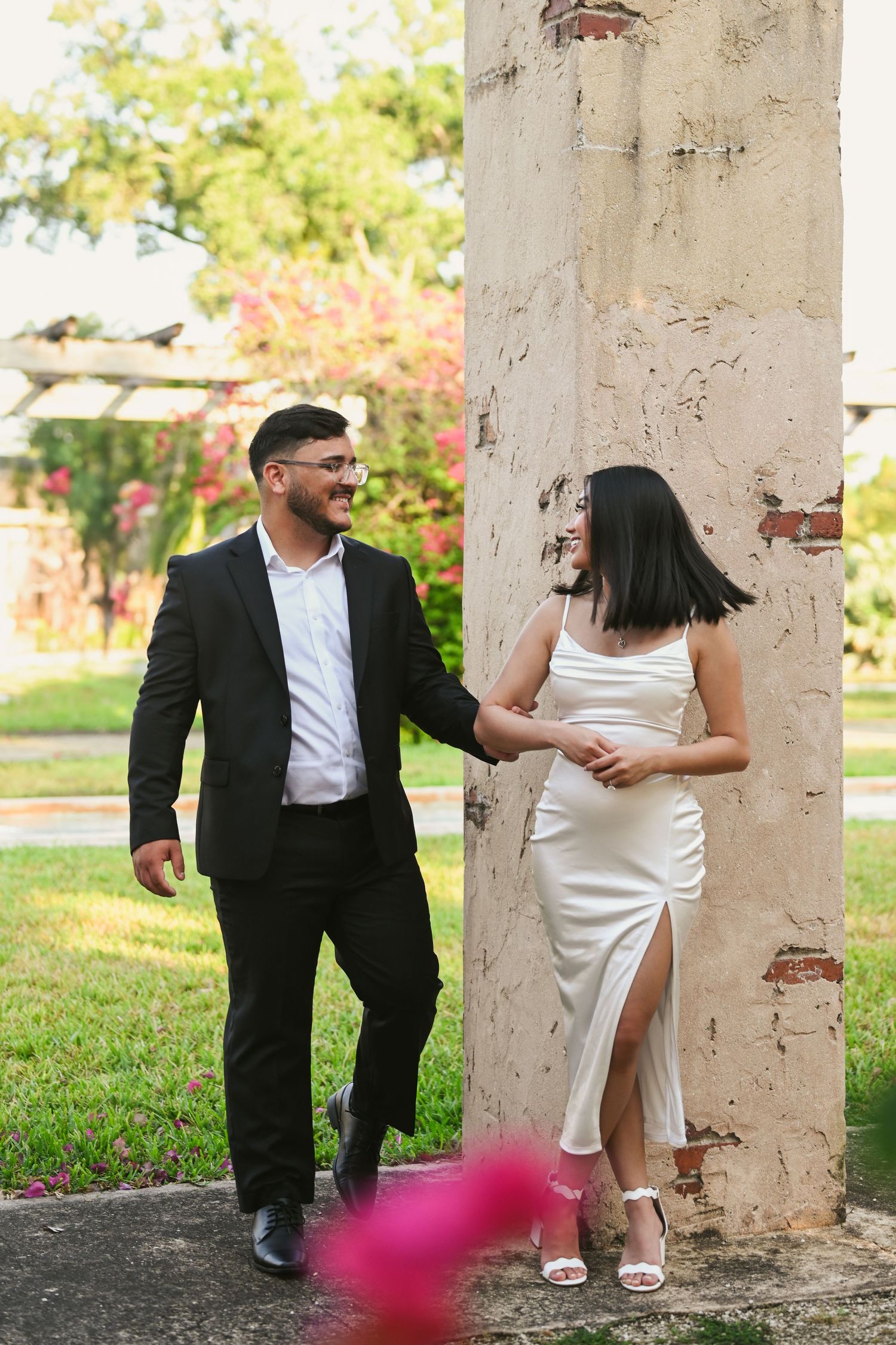 Couple in formal attire sharing a tender moment between weathered stone pillars.