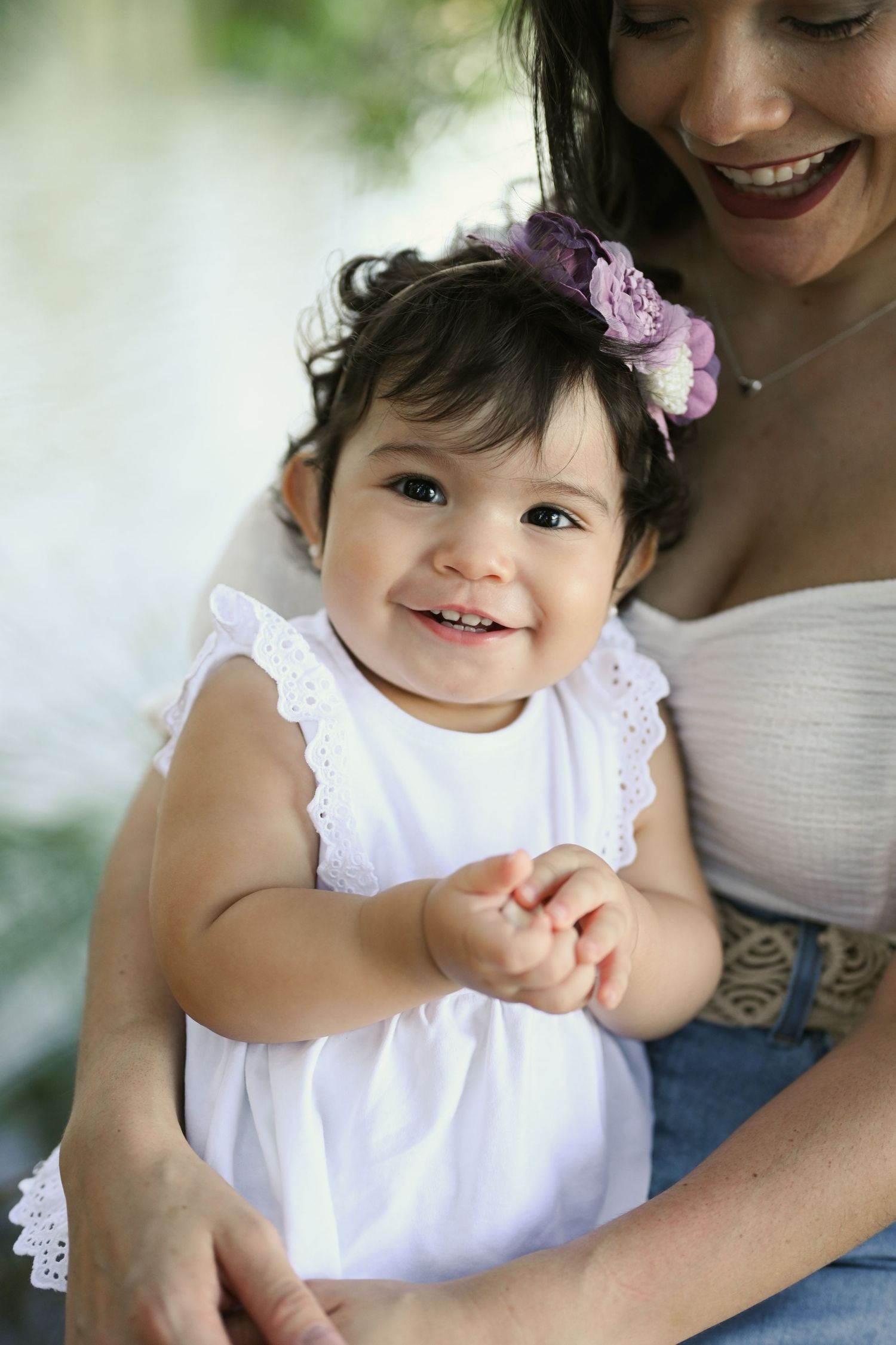 A happy child in a white dress smiles while being held in loving arms.