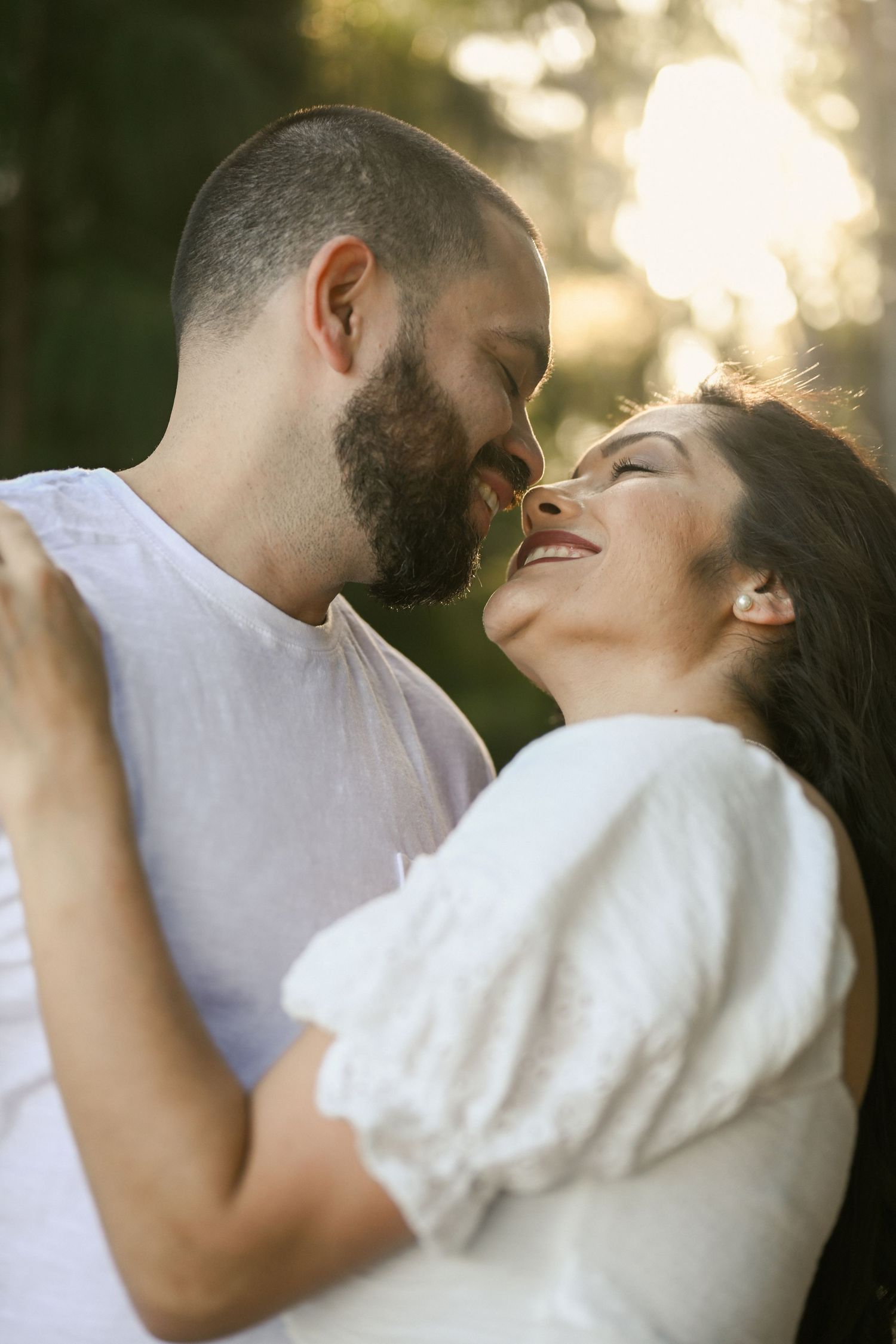 A loving couple shares romantic kisses in golden sunlight among trees.