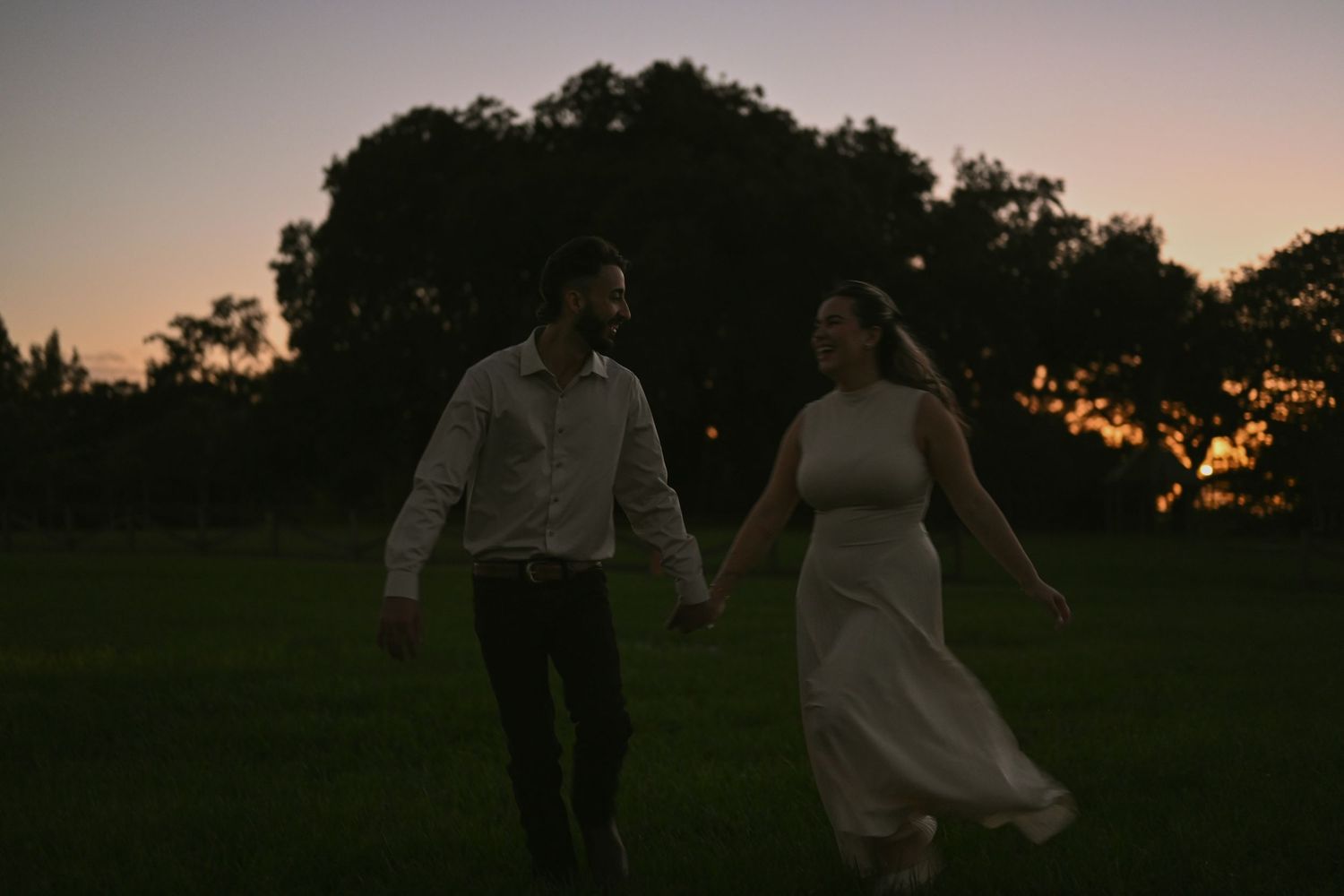 Silhouettes of a couple walking hand in hand against a dusky pink sky.