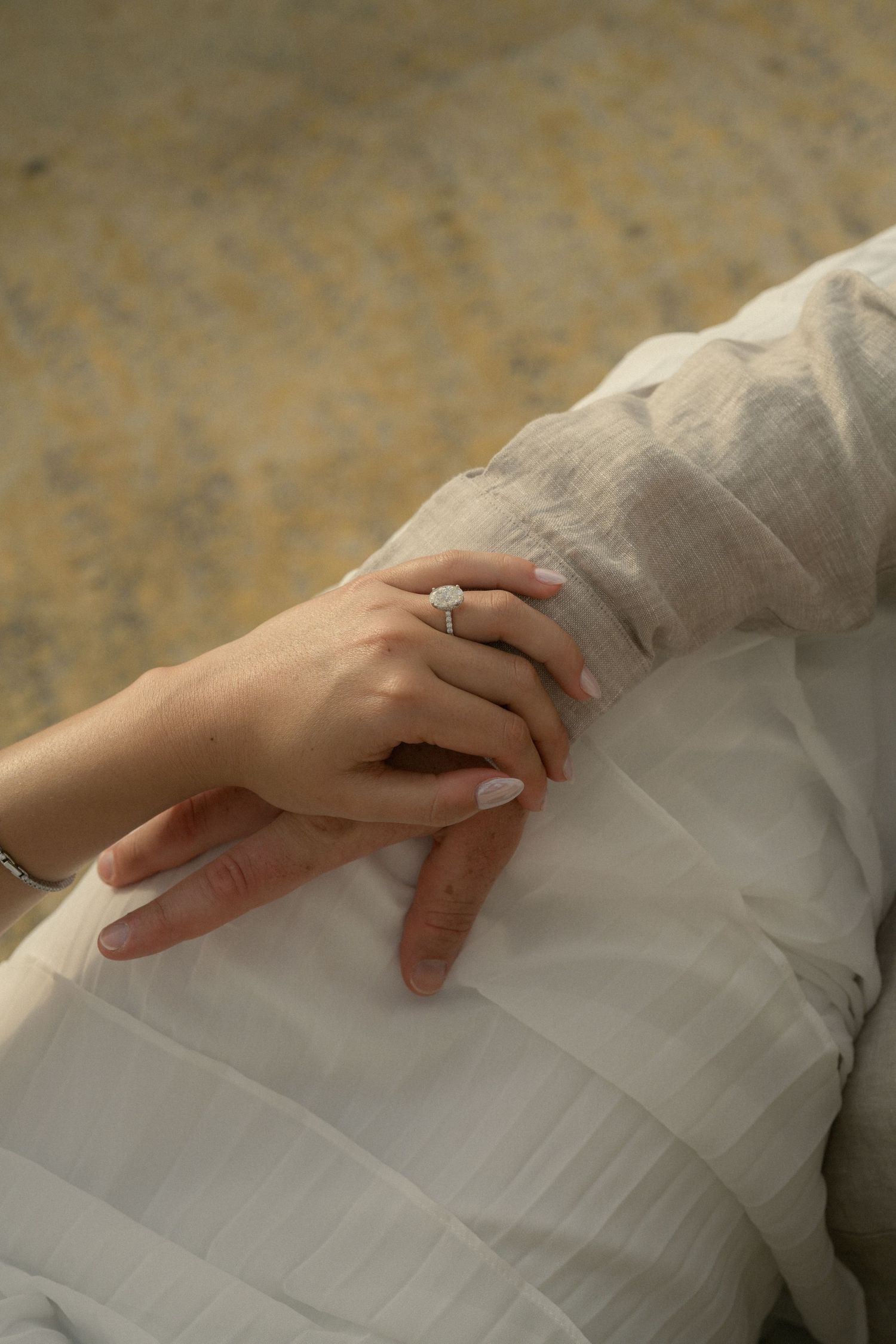 Close-up of elegant diamond engagement ring on bride's hand in white dress.