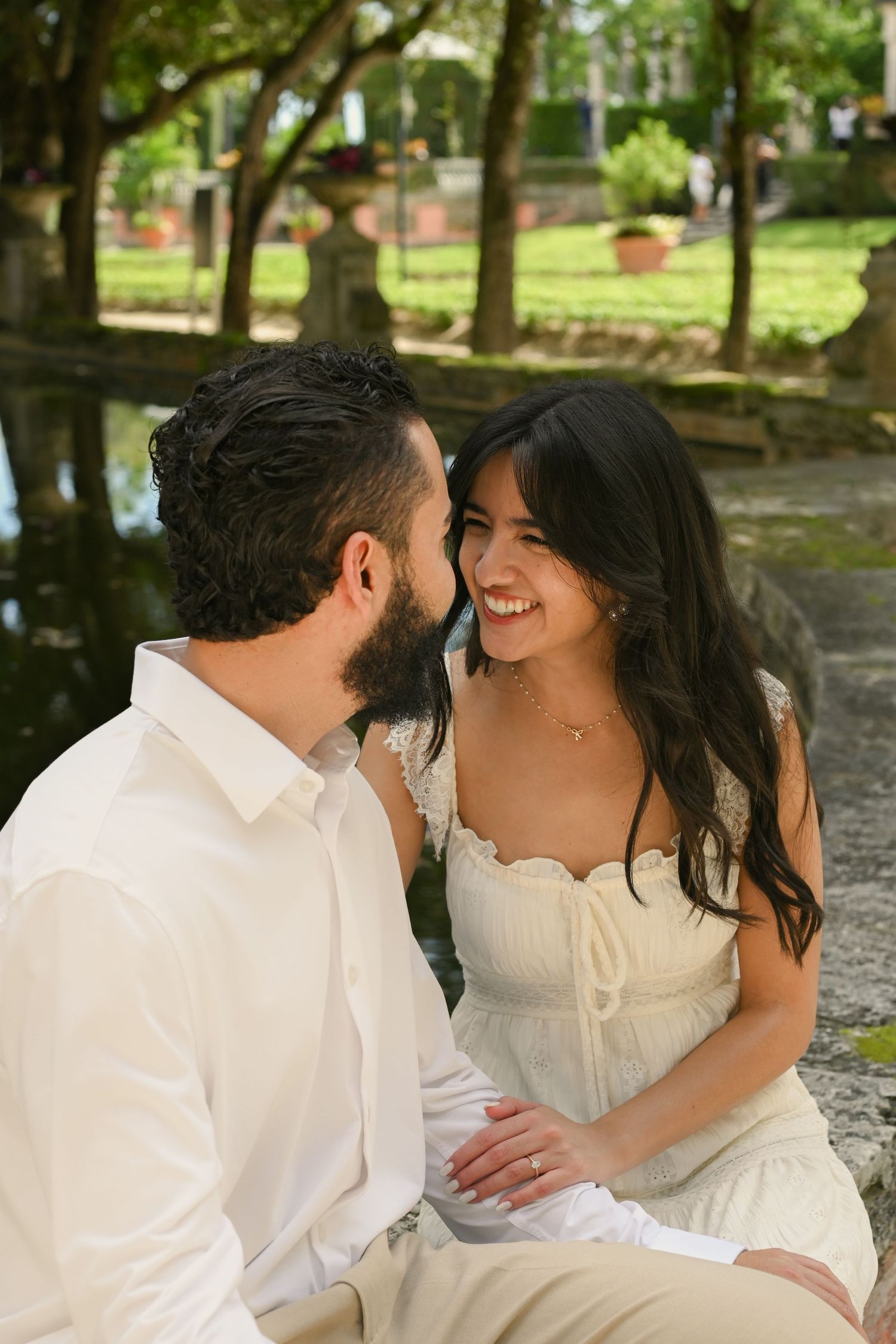 A couple in white attire shares joyful moments together in a sunlit outdoor park setting.