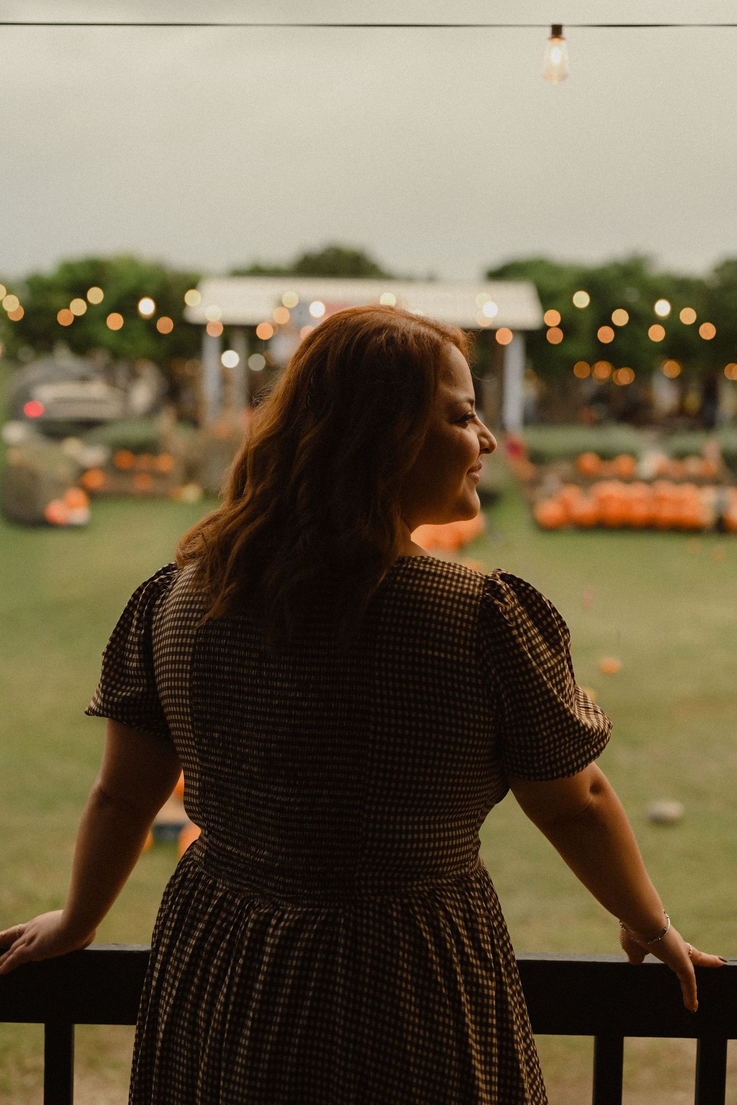A silhouette against a sunset sky with string lights and pumpkins in the background.