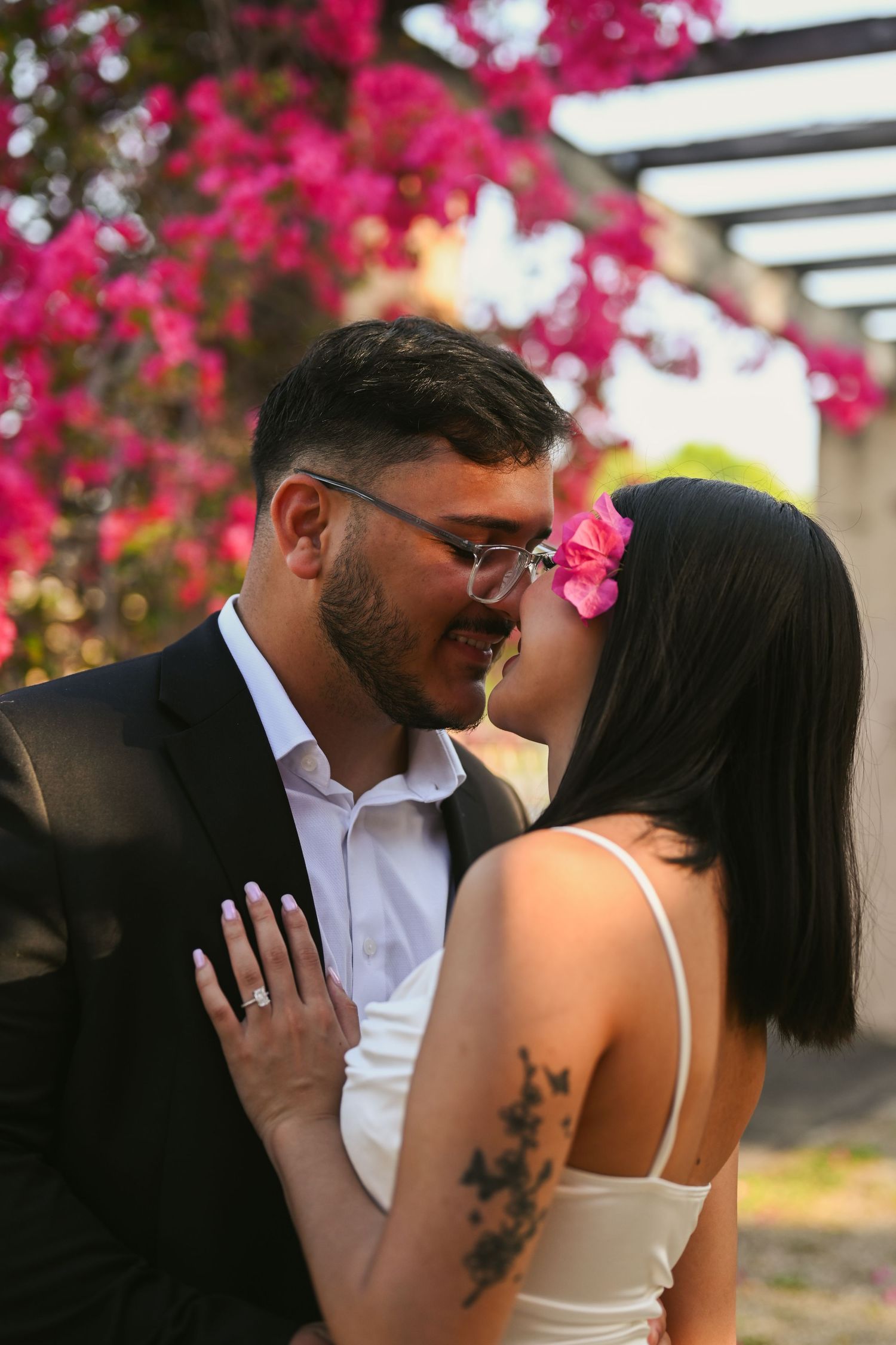 Romantic couple sharing intimate moments under vibrant pink bougainvillea flowers in an outdoor setting.