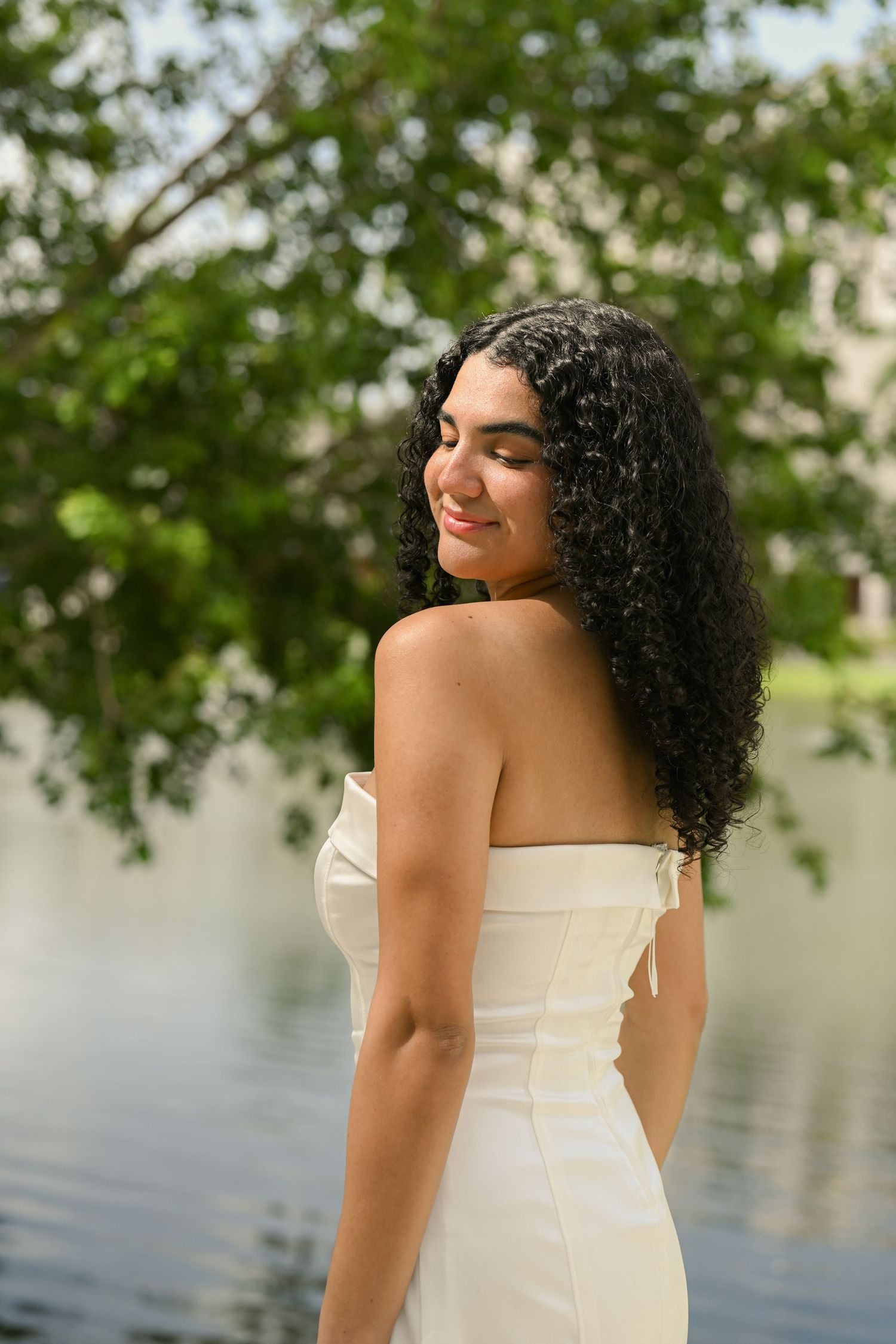 Outdoor graduation portrait session near a lake with green trees in background.