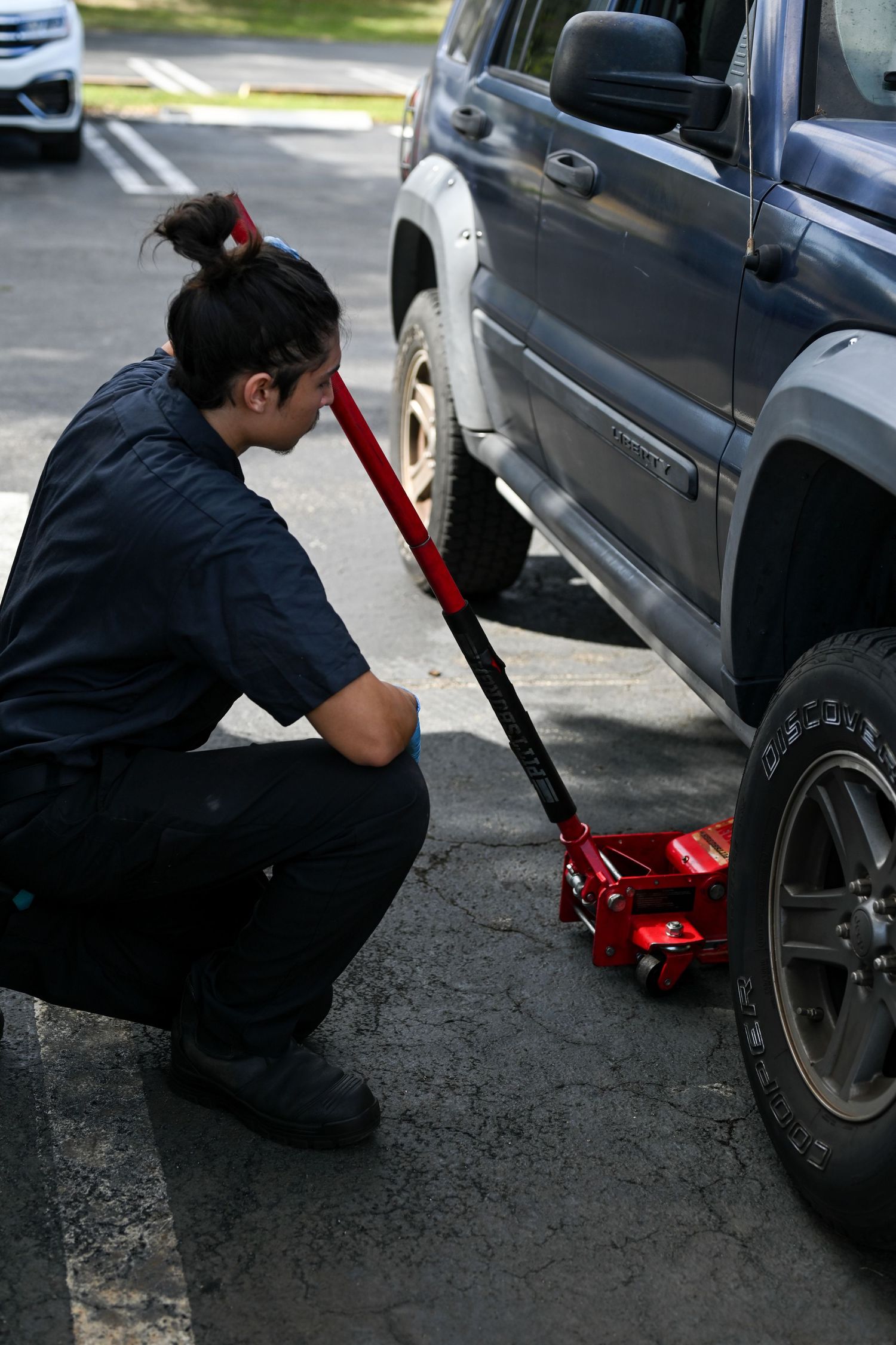 Service technician using a red floor jack to lift a vehicle.