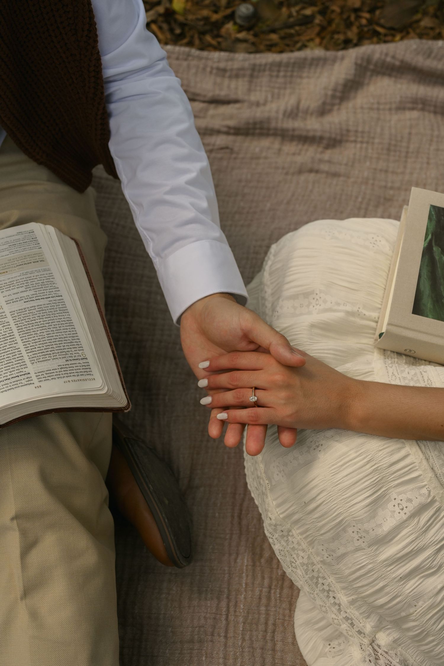 Hands rest on an open book with white lace fabric visible against a textured gray background.