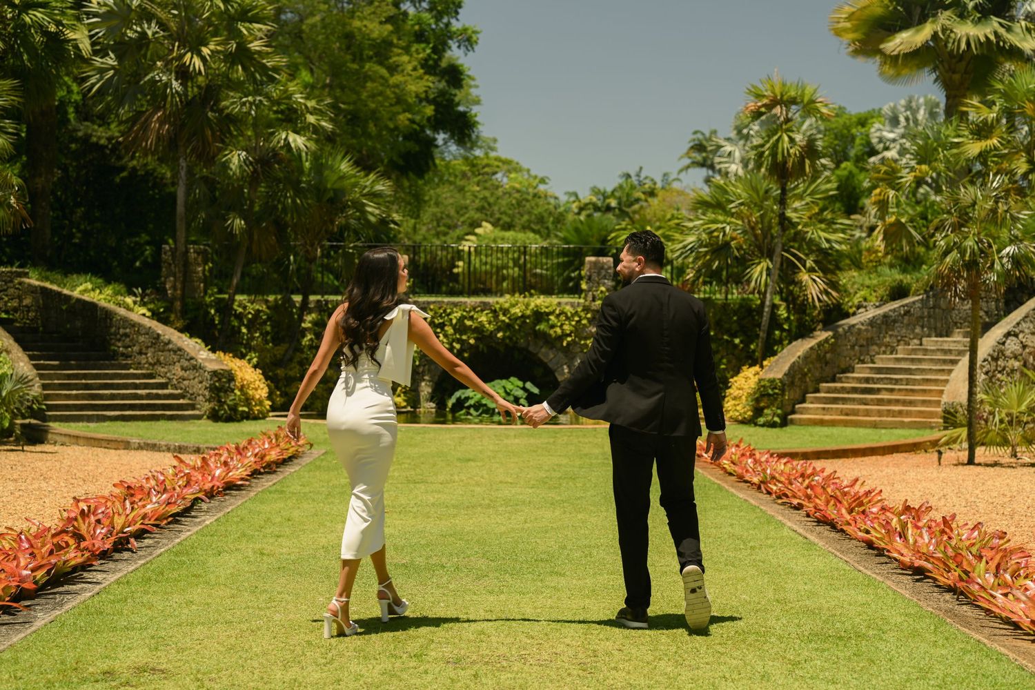 A couple poses playfully on a garden path lined with colorful flowers.