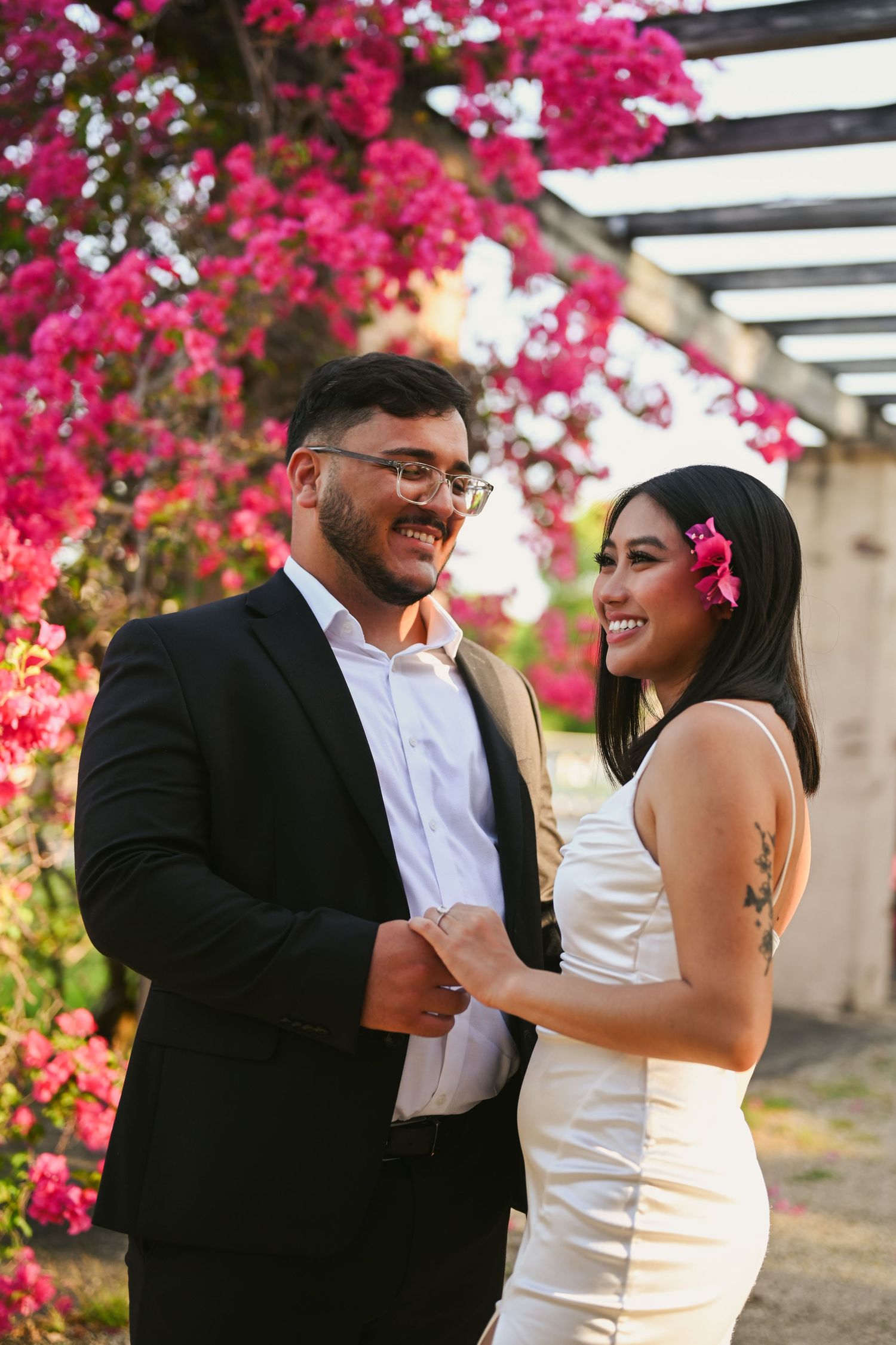A joyful couple sharing laughter beneath blooming pink bougainvillea flowers in an outdoor setting.