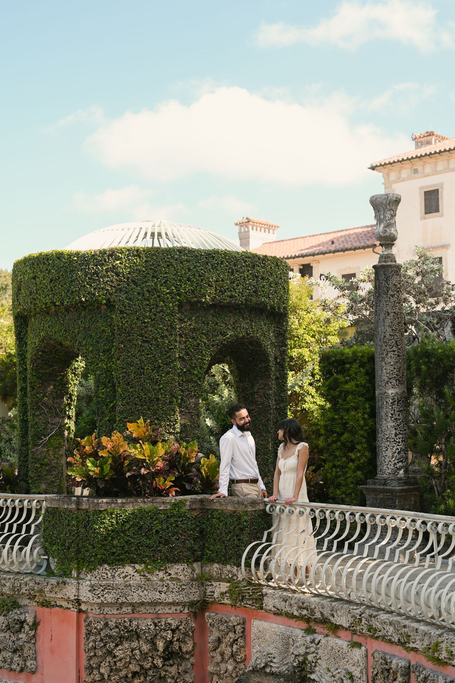 Couple in wedding attire standing on ivy-covered terrace at Vizcaya Museum and Gardens in Miami.