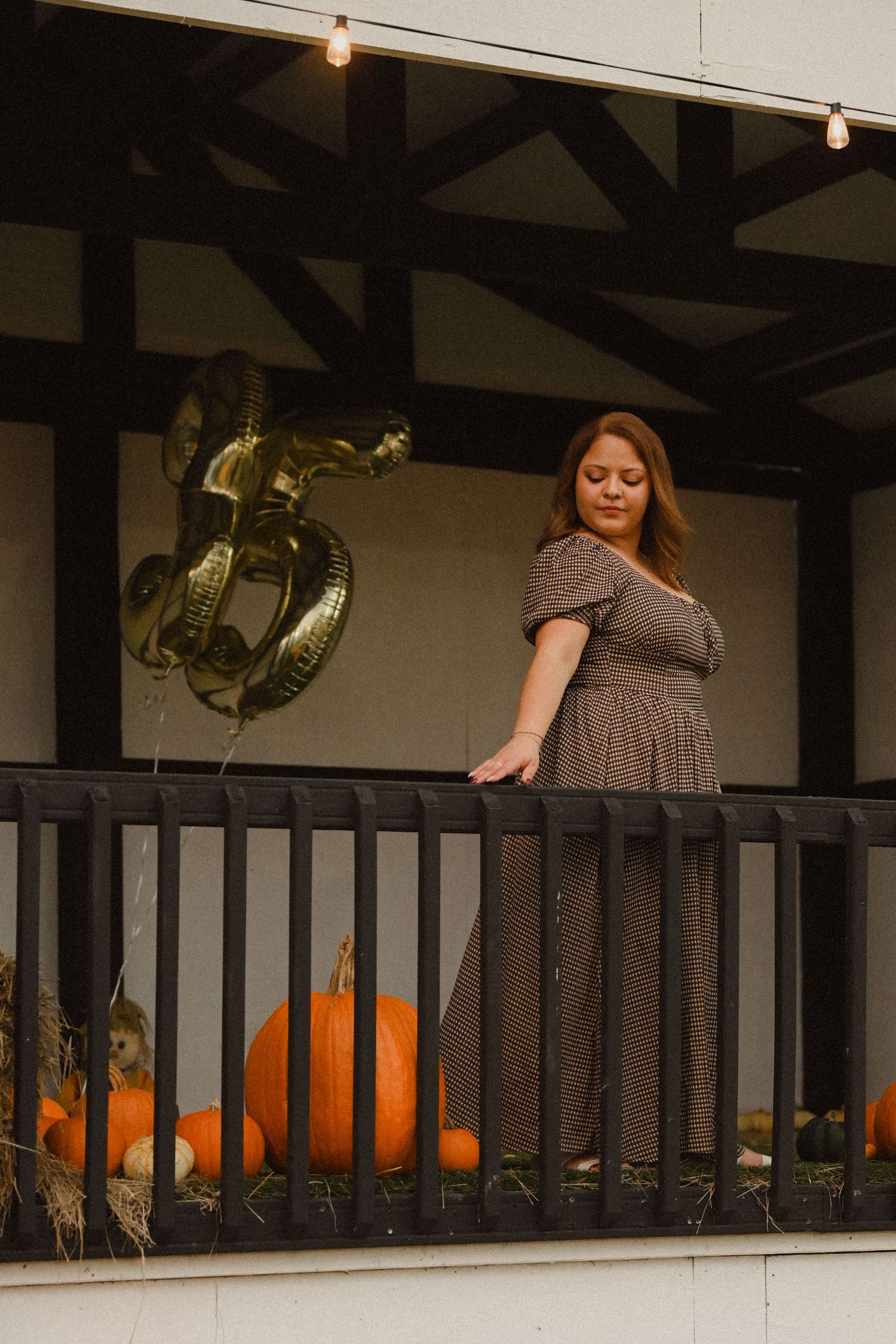 Dark wooden balcony decorated with string lights and orange pumpkins for fall season.