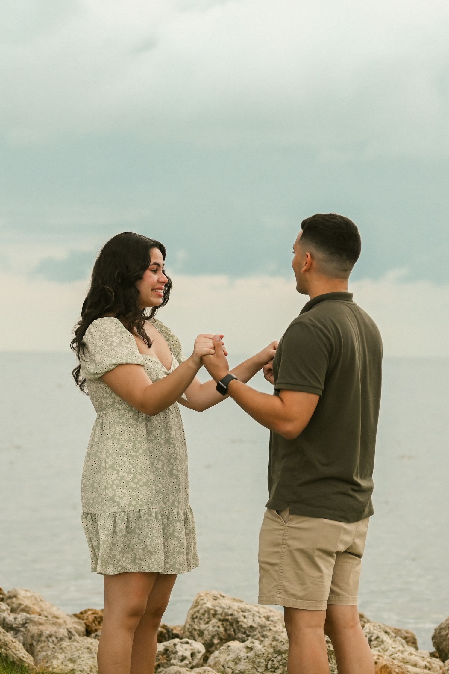 A couple holds hands while standing on a coastal cliff overlooking the ocean.