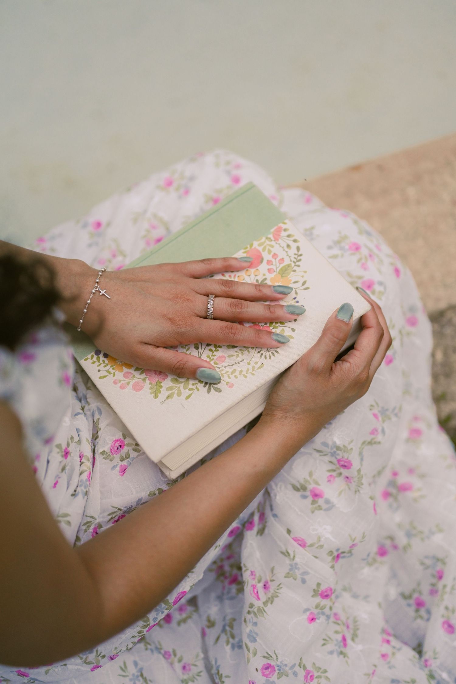 Hands with painted nails and jewelry hold open pages of a book against a floral dress.