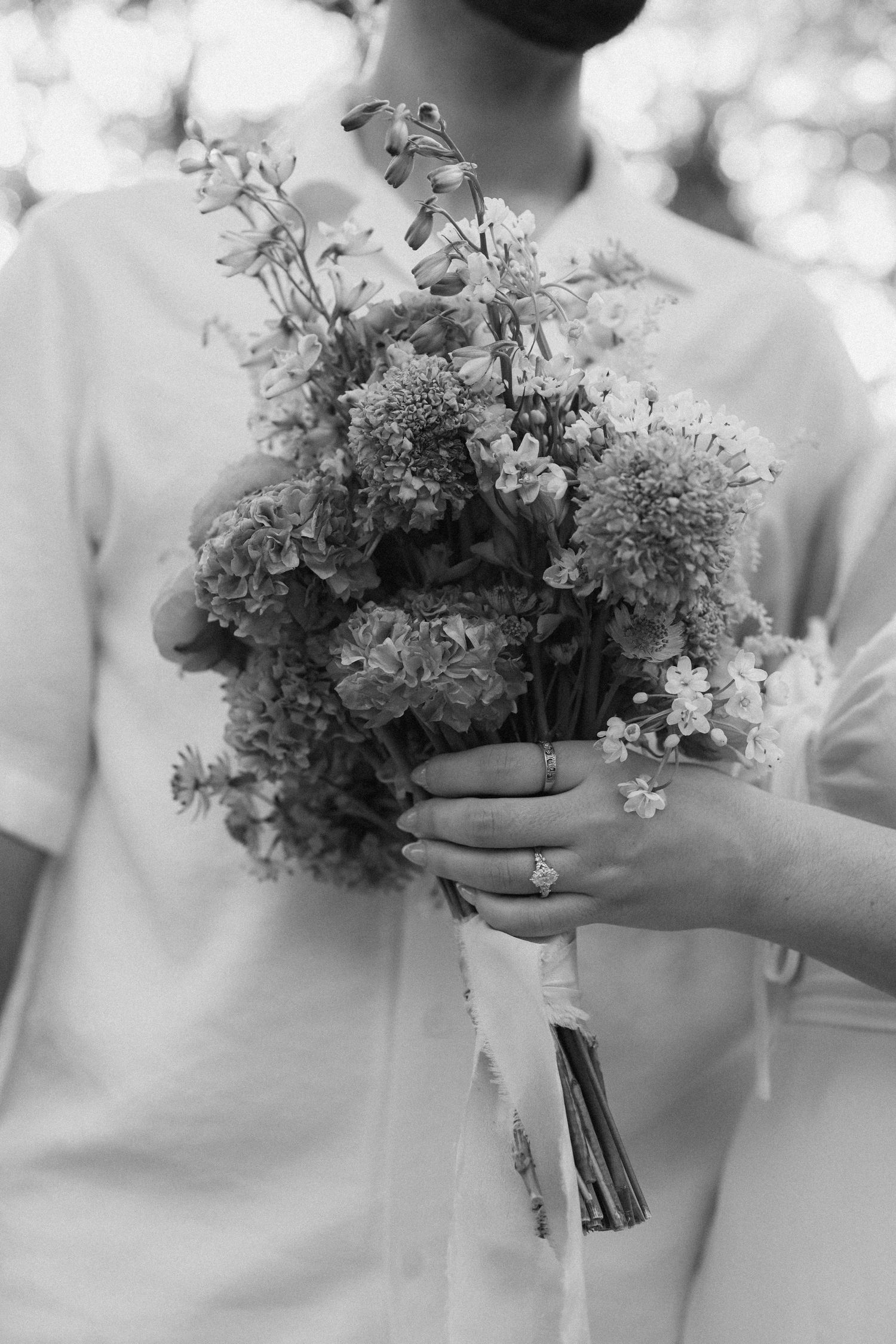 Black and white photo of a bride and groom holding a wildflower wedding bouquet with ribbon.