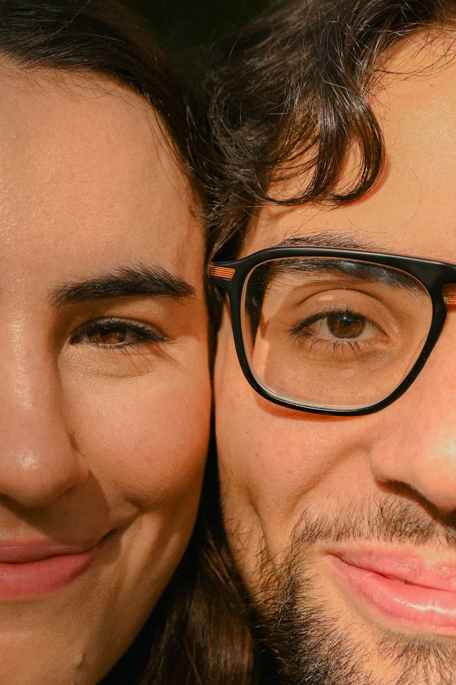 Close-up portrait of a couple smiling at camera, one wearing black-framed glasses.
