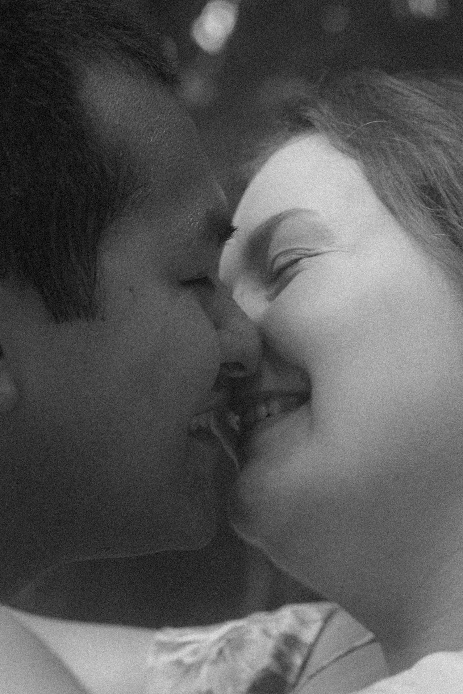 Black and white photo of a smiling couple sharing a romantic moment, nearly kissing in an outdoor setting.