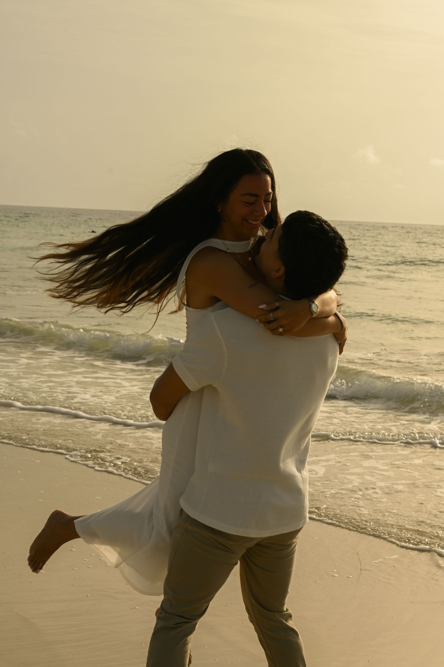A couple spins in a romantic dance pose on the beach with flowing hair in the wind.