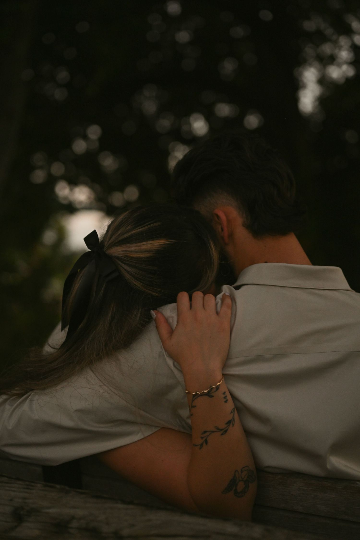 Close-up shot of tender embrace on wooden bench in natural setting.