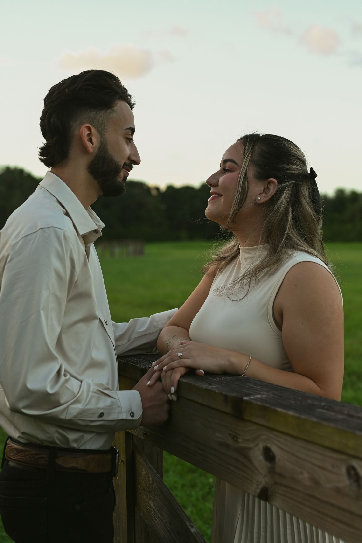 A couple shares an intimate moment while leaning against a wooden railing in a park at dusk.