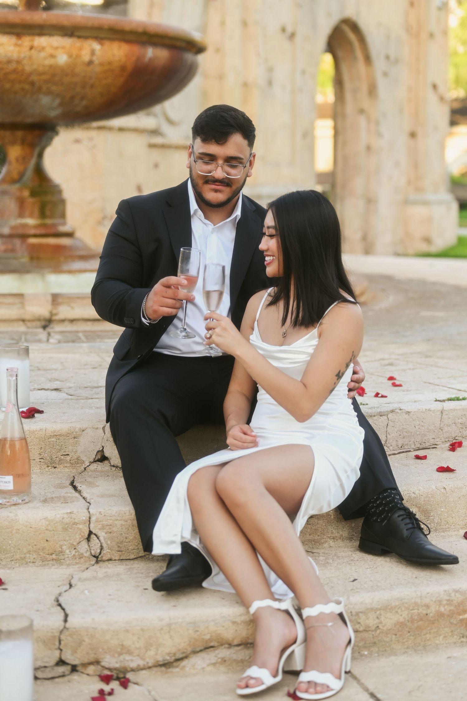 Couple sitting on stone steps sharing drinks and laughter in an outdoor setting.