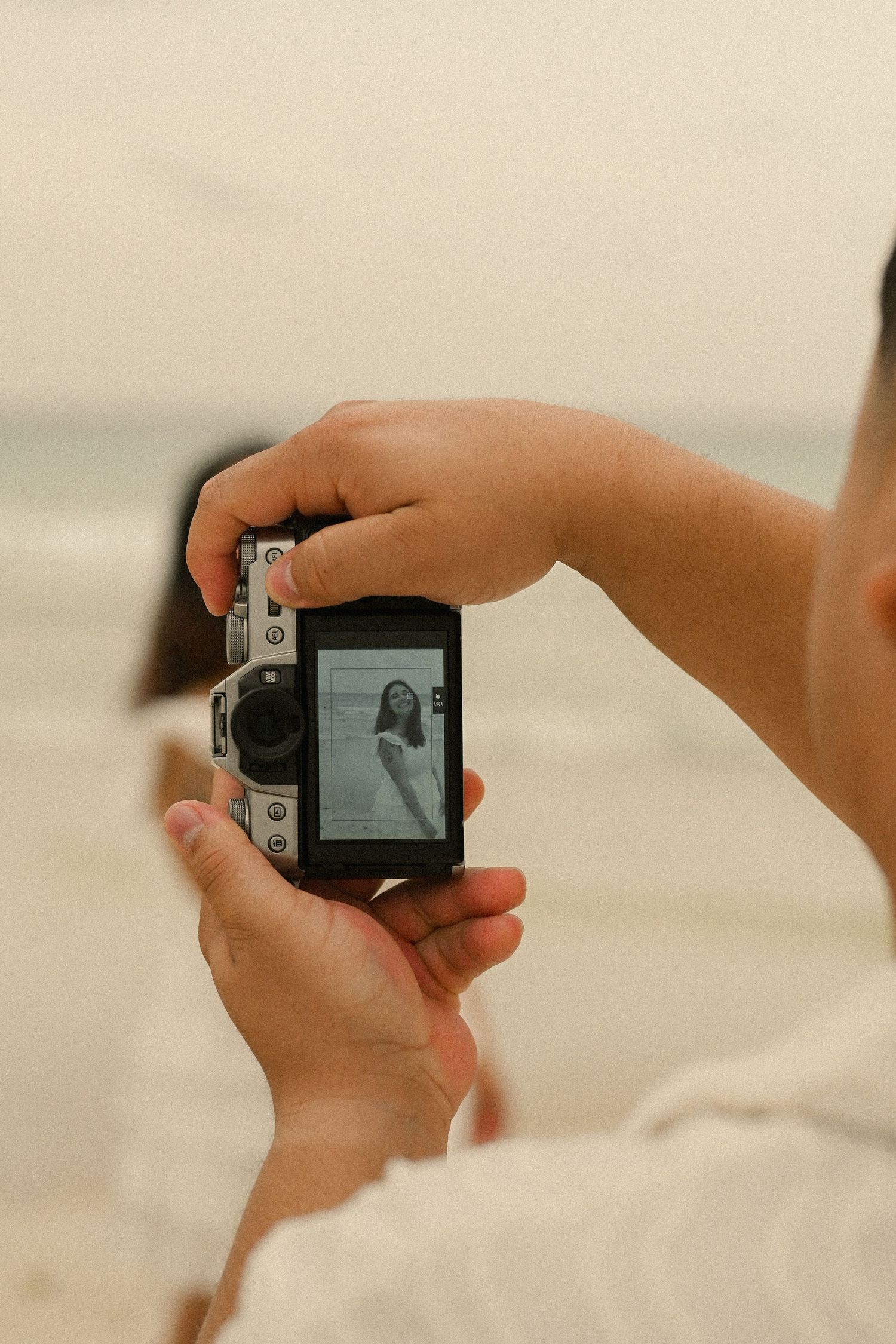 Hands hold a vintage camera on the beach, capturing memories in a nostalgic style.