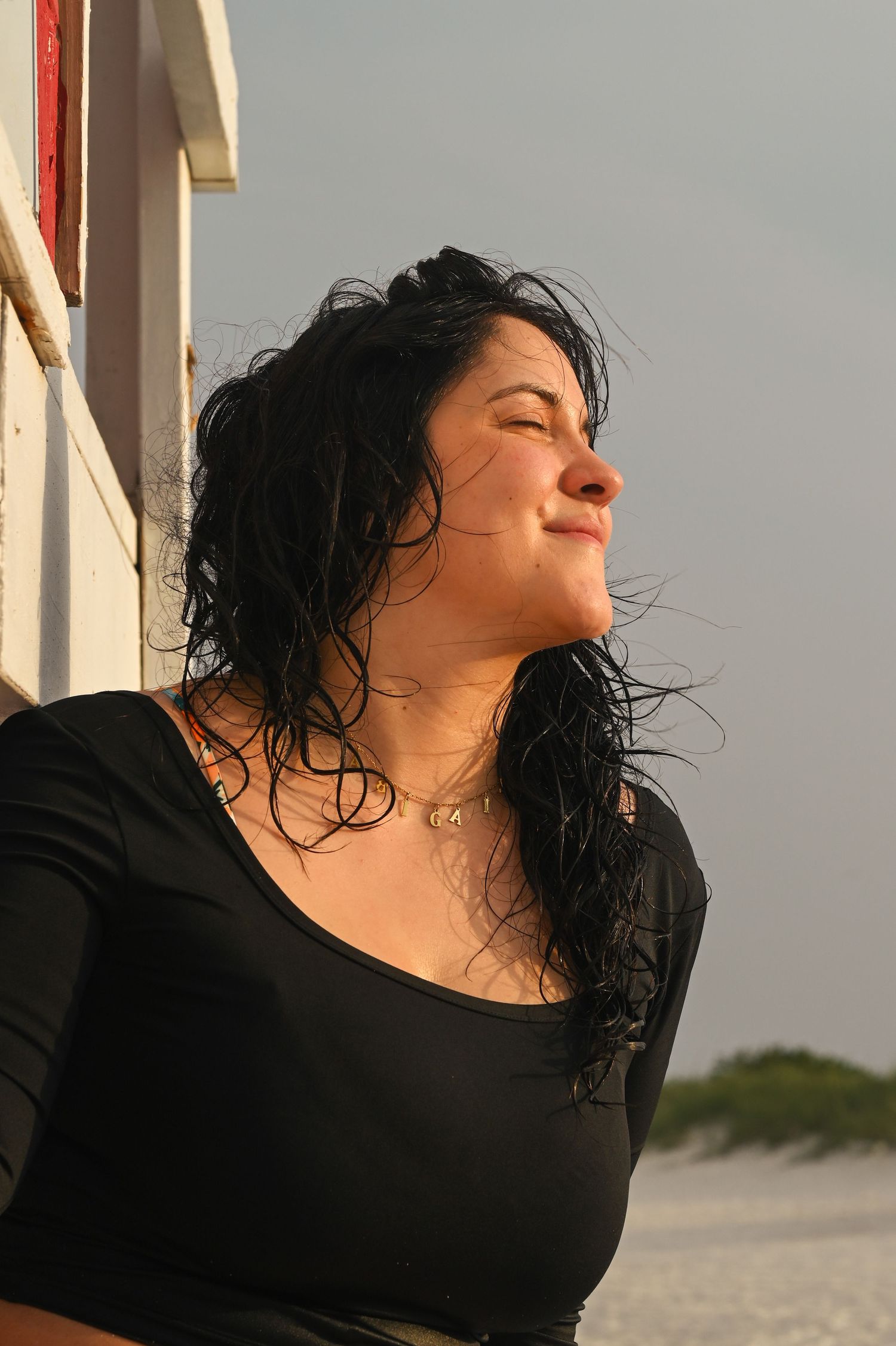 Person with wet dark hair wearing black top poses against sunset sky.