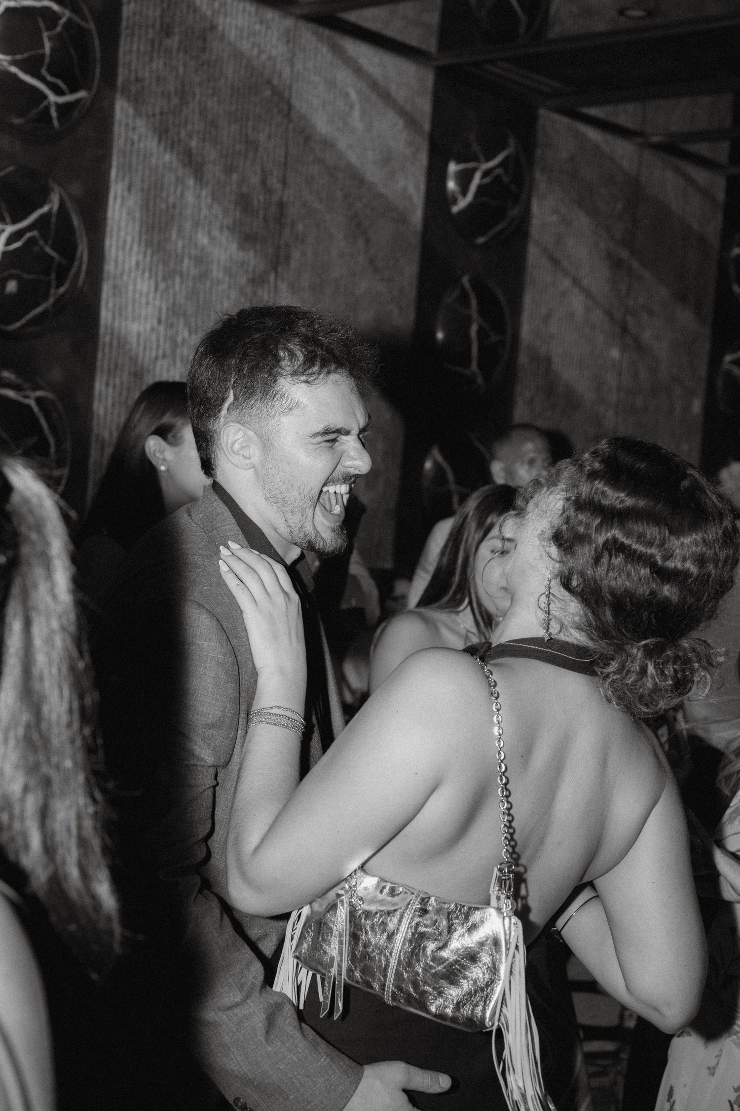Black and white photo of a laughing man and woman dancing together at a lively nightclub party event.