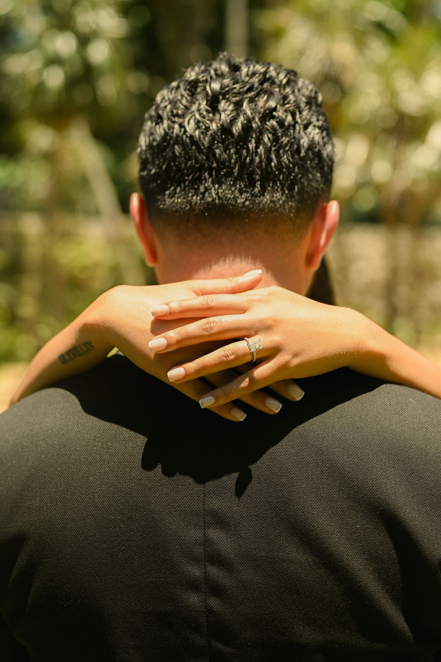 Close-up shot showing hands resting on the back of someone wearing a black suit.