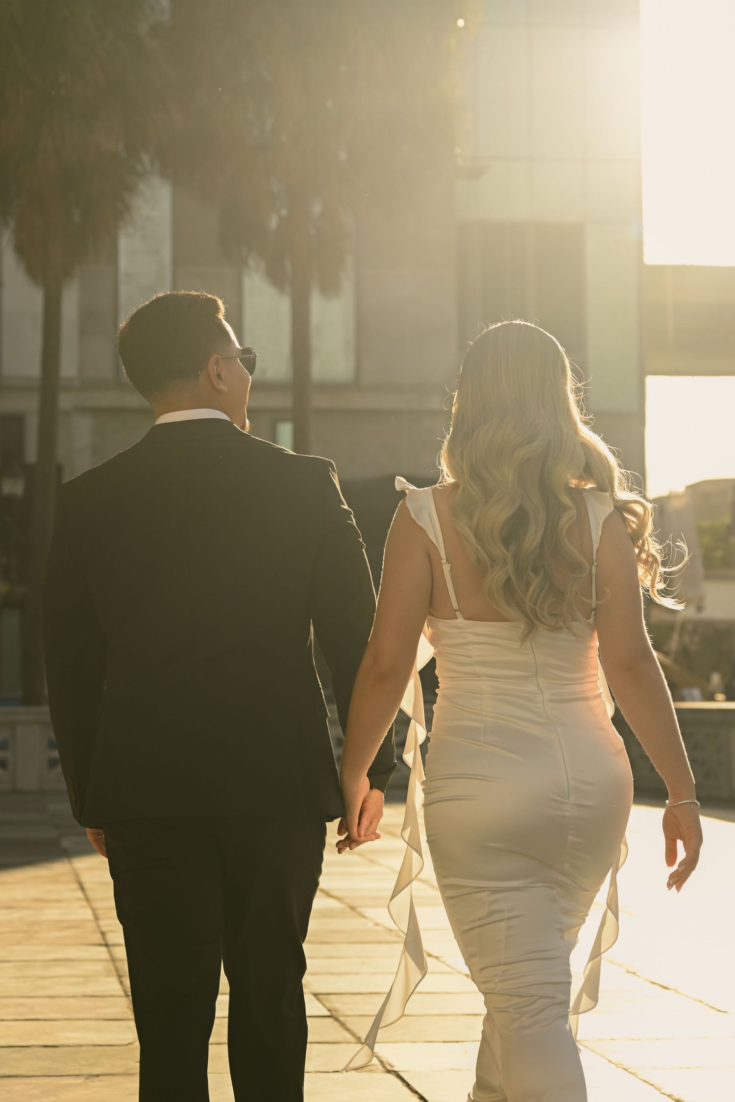 Couple walks hand in hand during sunset wedding photoshoot at historic venue.