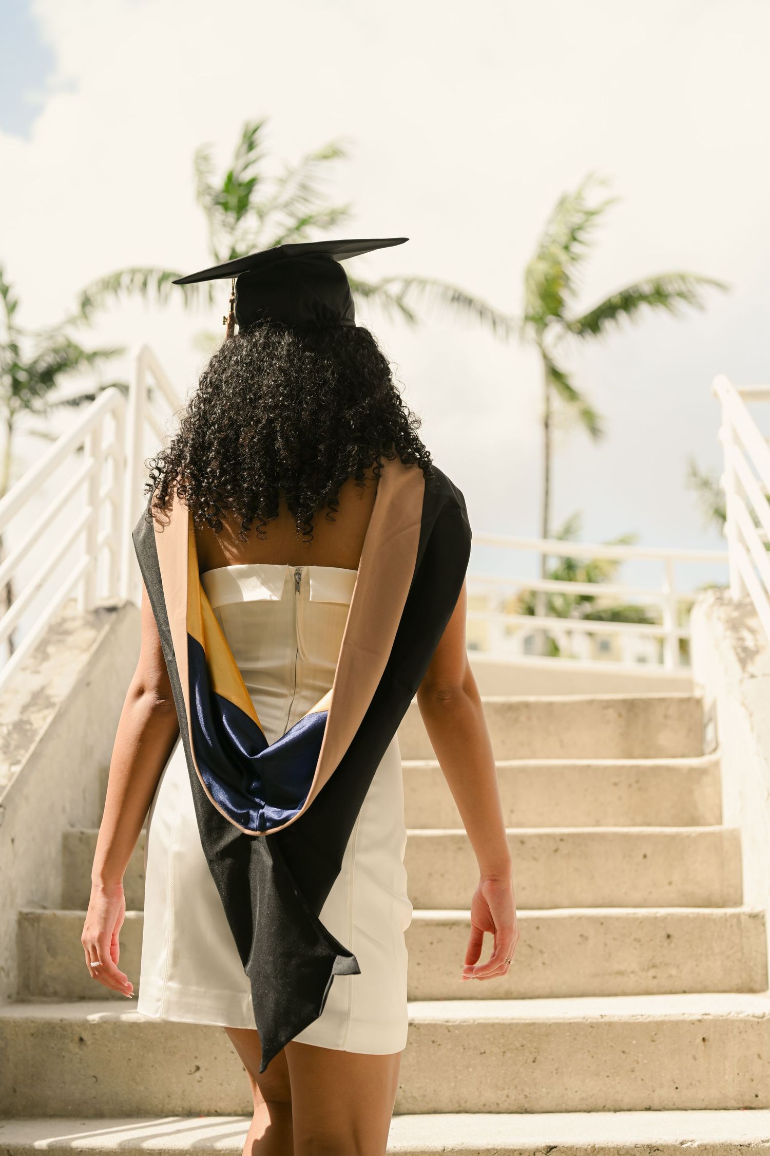 Graduate ascending concrete steps in cap and gown during sunny photo session.