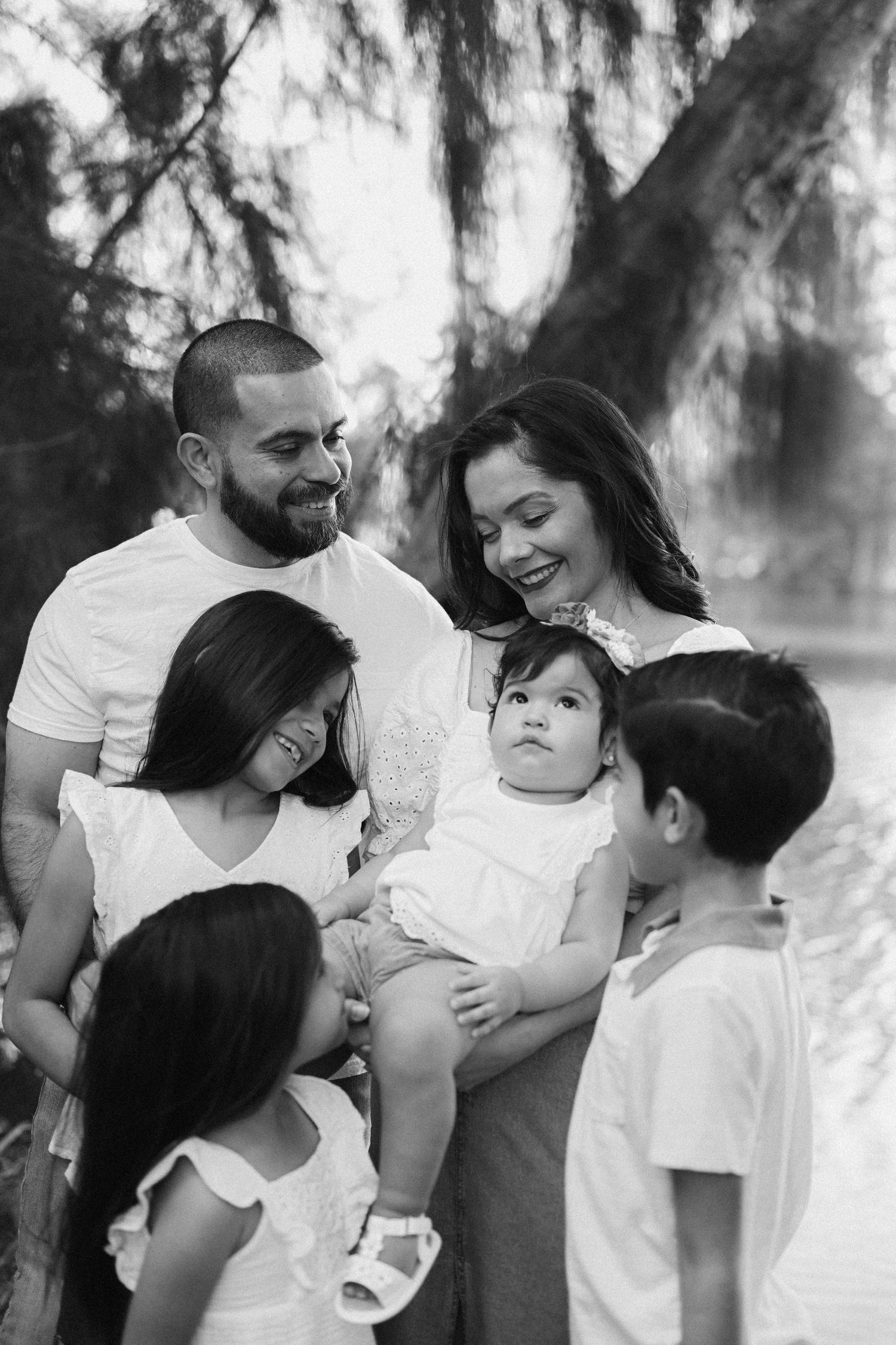 Family wearing white outfits sharing intimate moments together in a forest setting.